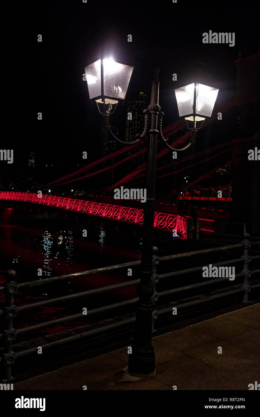 Classic street lampade davanti al ponte Cavenaugh, la sola sospensione ponte sul fiume Singapore, illuminato in rosso la notte. Foto Stock
