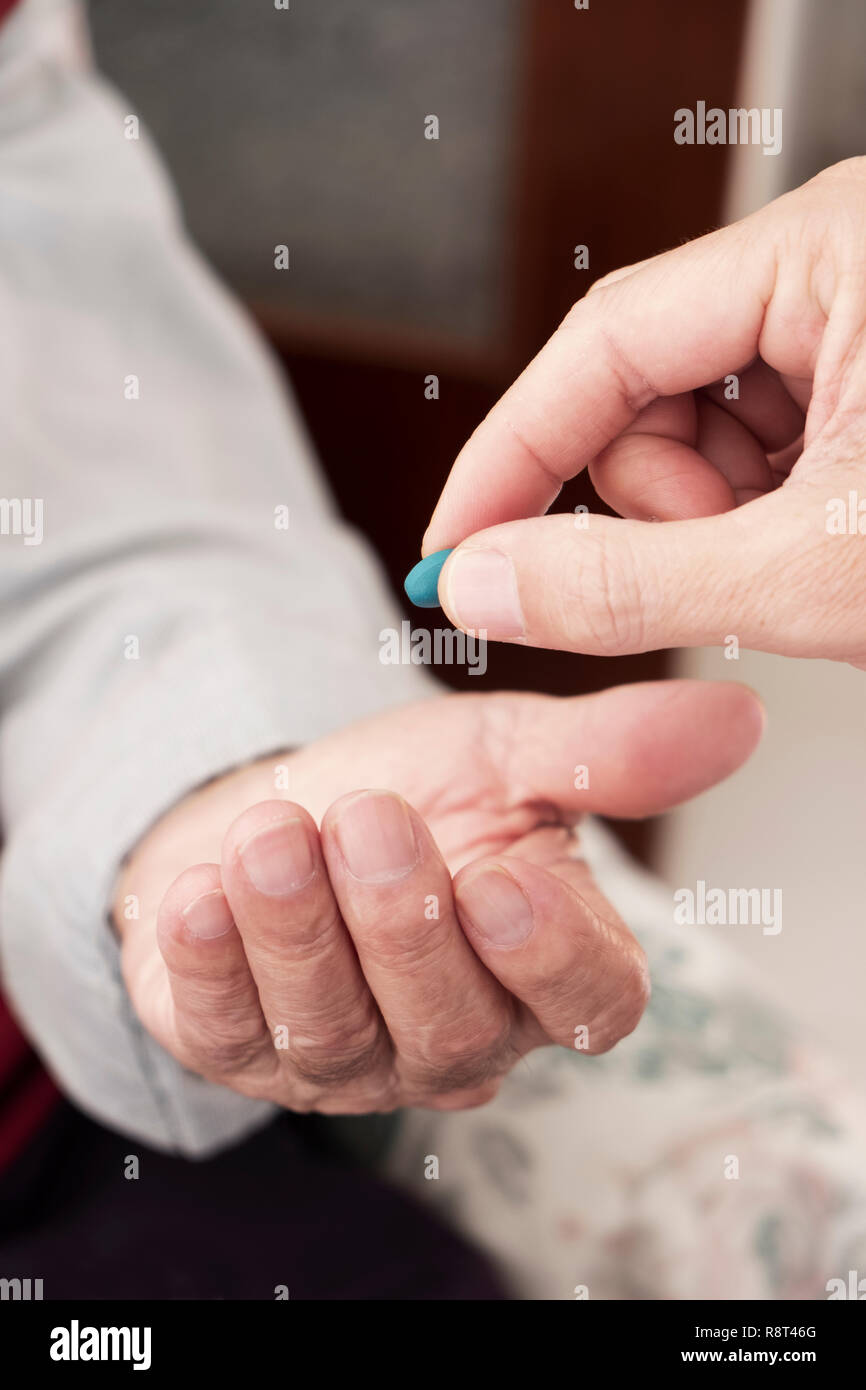 Primo piano di un medico caucasica uomo in camice bianco, dando una pillola blu a un senior caucasica uomo paziente, a casa sua o in una casa di cura Foto Stock