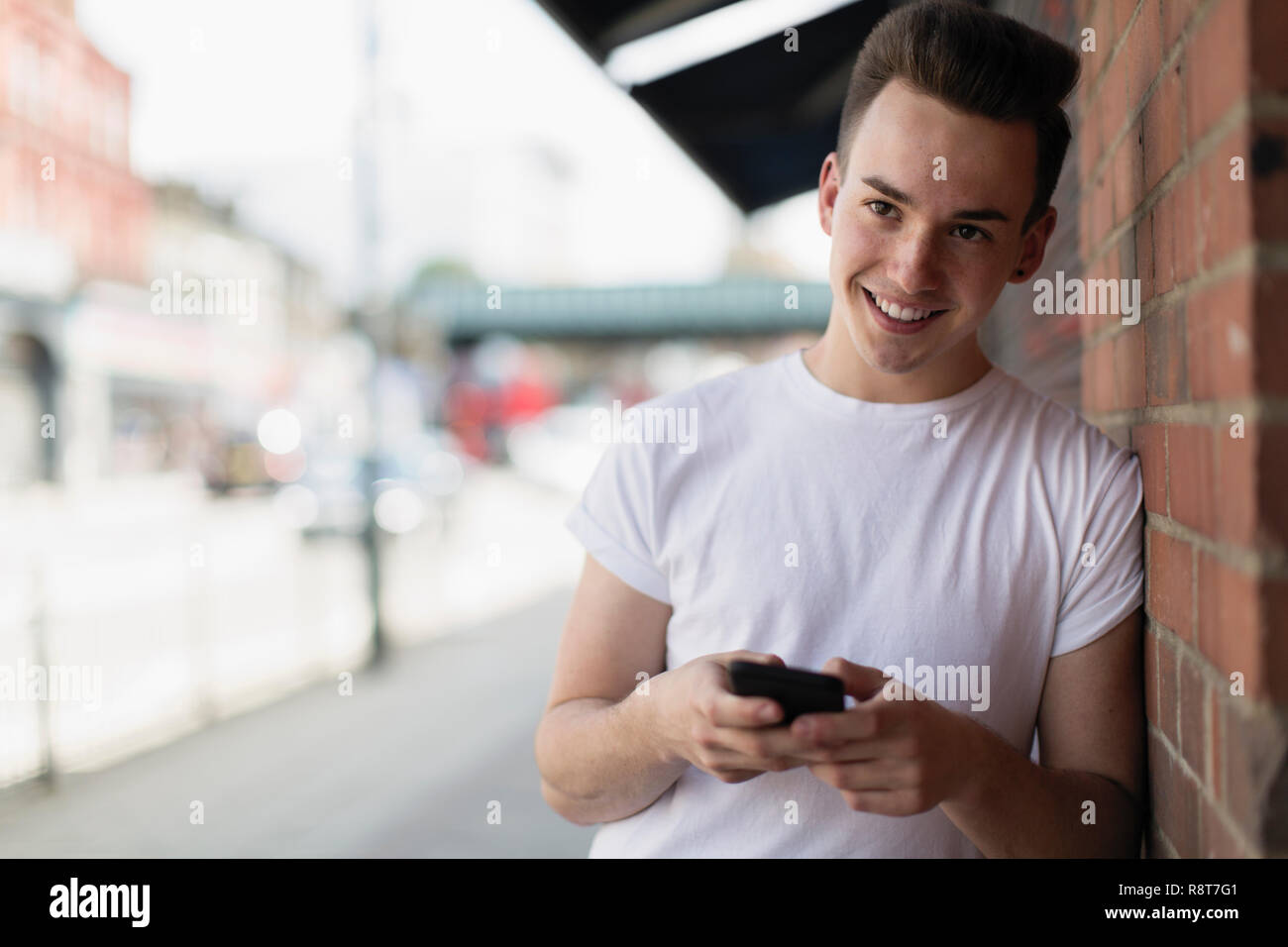 Ragazzo adolescente utilizzando smart phone sul marciapiede urbano Foto Stock