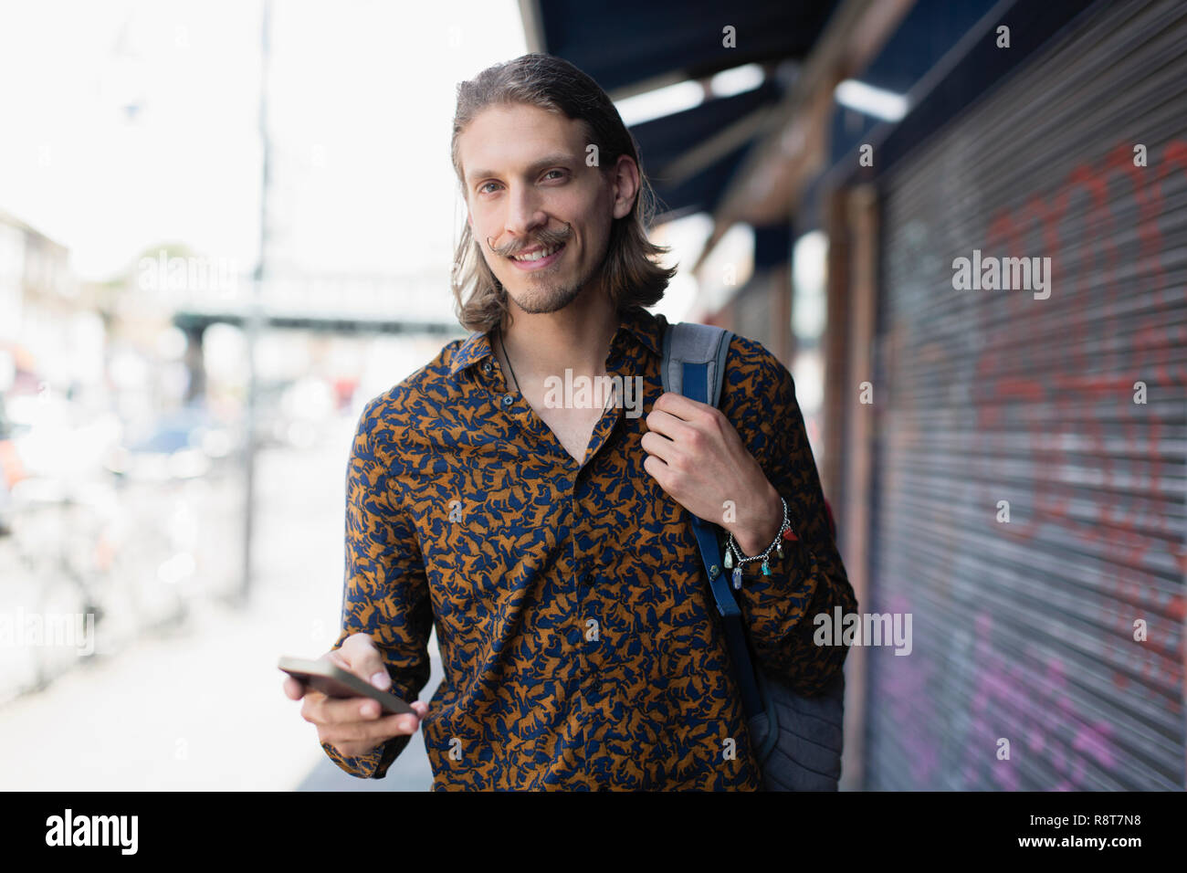 Ritratto fiducioso hipster uomo con smart phone sul marciapiede urbano Foto Stock