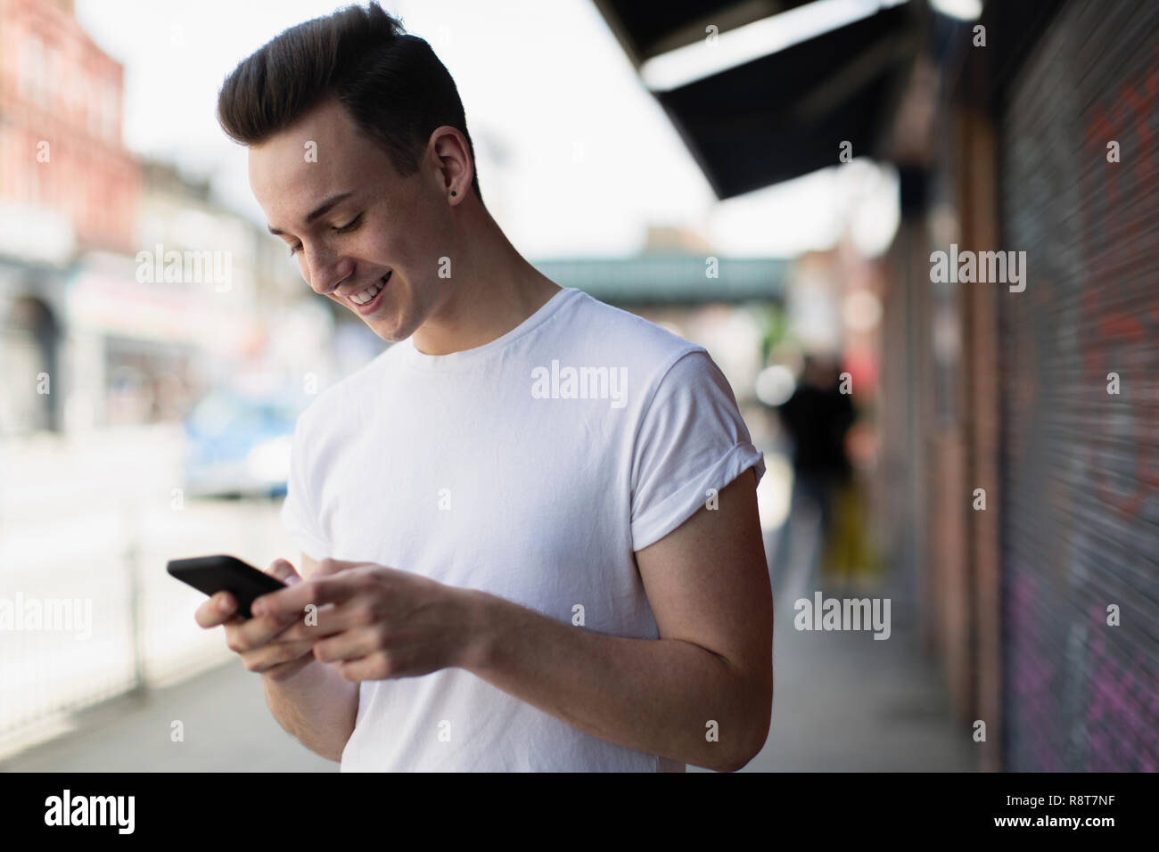 Sorridente ragazzo adolescente utilizzando smart phone sul marciapiede urbano Foto Stock