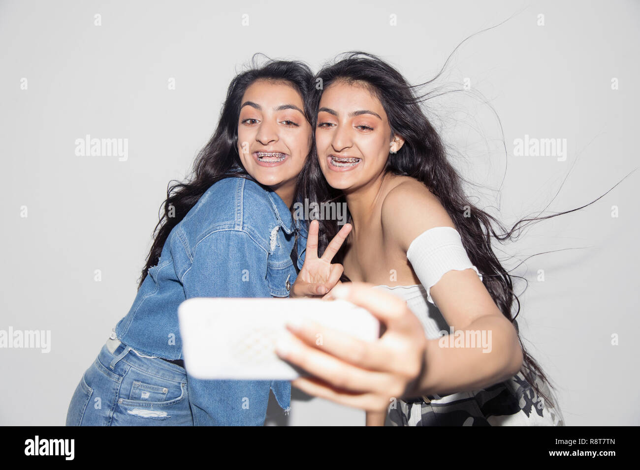 Carefree teenage gemelle con bretelle tenendo selfie con smart phone Foto Stock