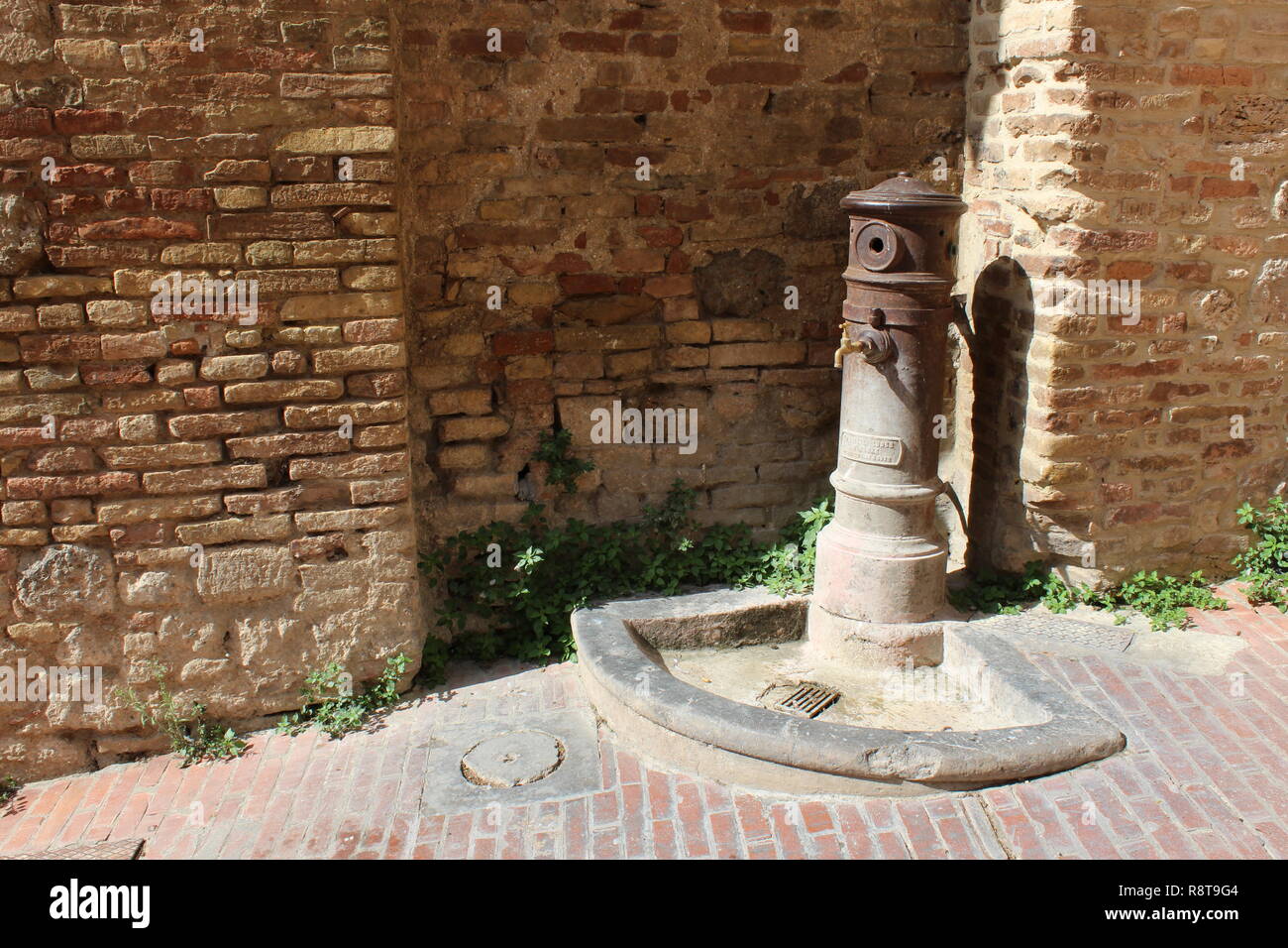 Fontanella di fronte a un vecchio muro in San Gimignano, Italia Foto Stock