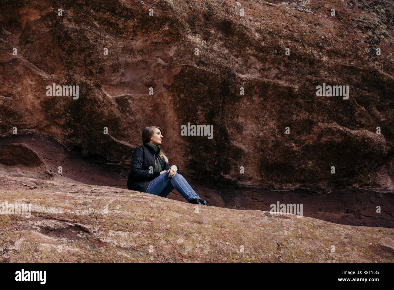 Giovani carino caucasico moderna donna sorridente di fronte all imponente naturale di roccia rossa muro di pietra al di fuori in natura presso il parco dello stato Foto Stock