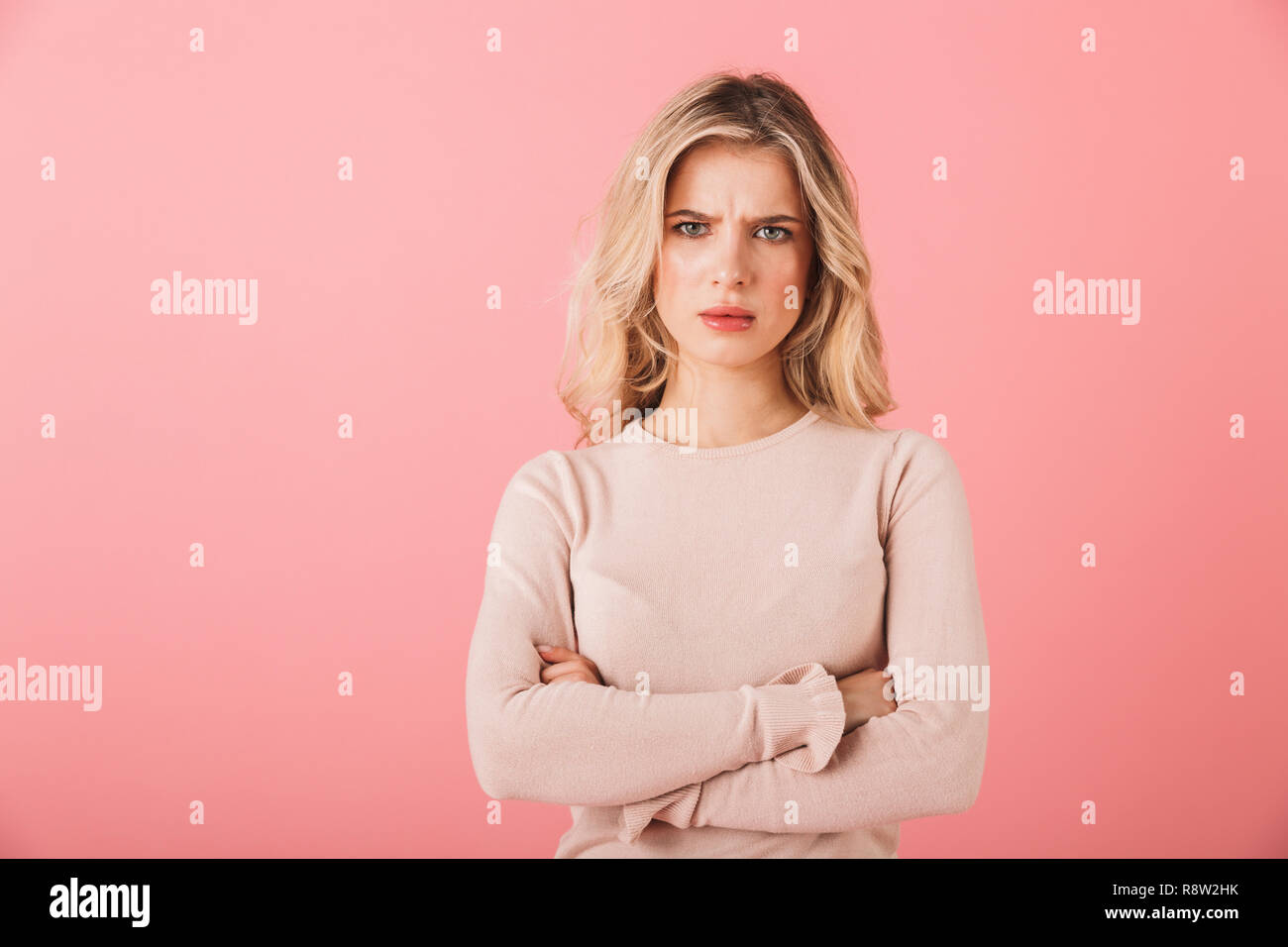 Ritratto di un giovane arrabbiato donna che indossa un maglione in piedi isolato su sfondo rosa, bracci ripiegati Foto Stock