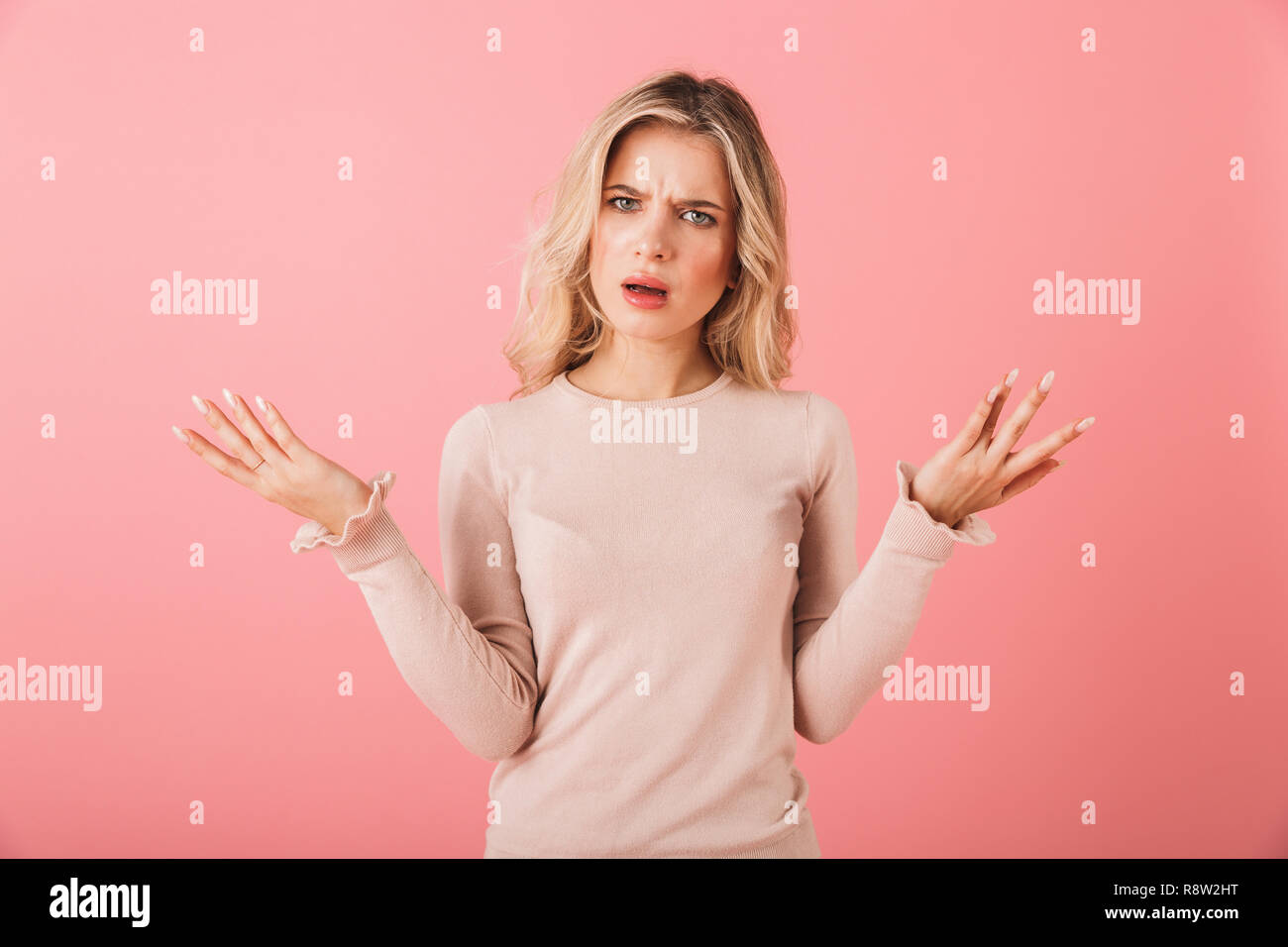 Ritratto di un giovane arrabbiato donna che indossa un maglione in piedi isolato su sfondo rosa, scrollare le spalle Foto Stock