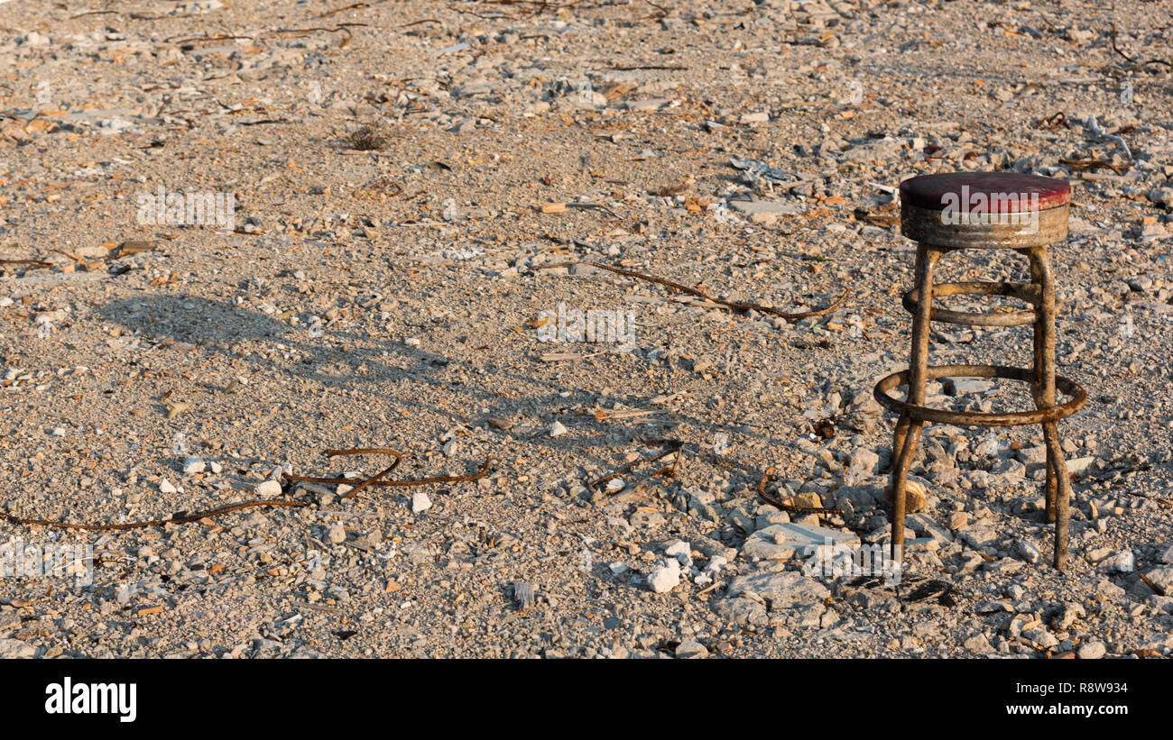 Una vecchia sedia bar da solo su un pavimento in cemento con una lunga ombra Foto Stock