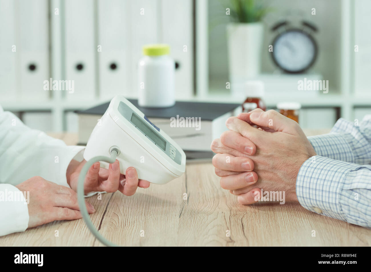 Il medico e il paziente con digital monitor della pressione del sangue in ufficio medico, close up delle mani Foto Stock