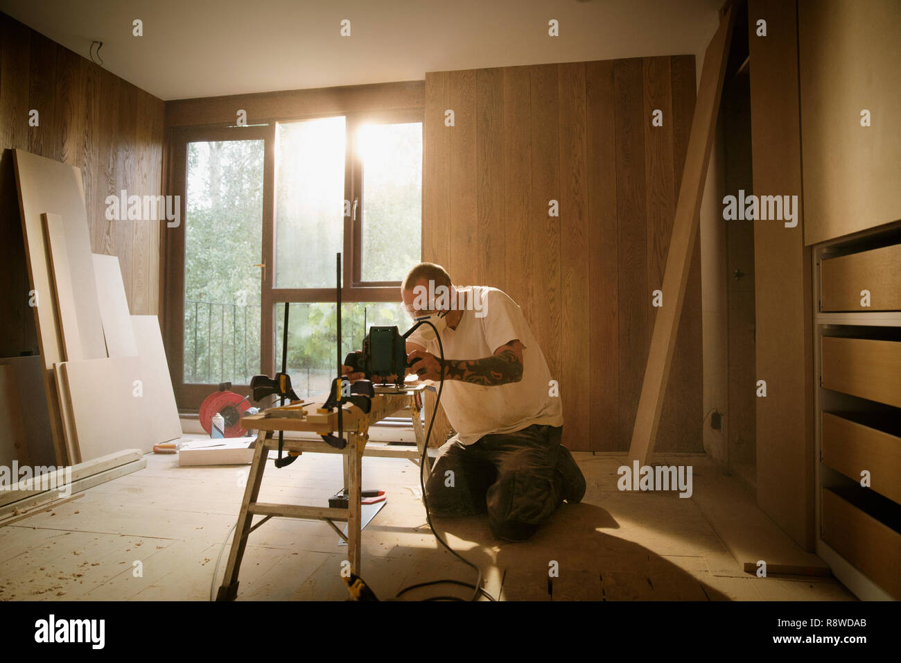 Lavoratore edile con sega elettrica per tagliare il legno in casa Foto Stock