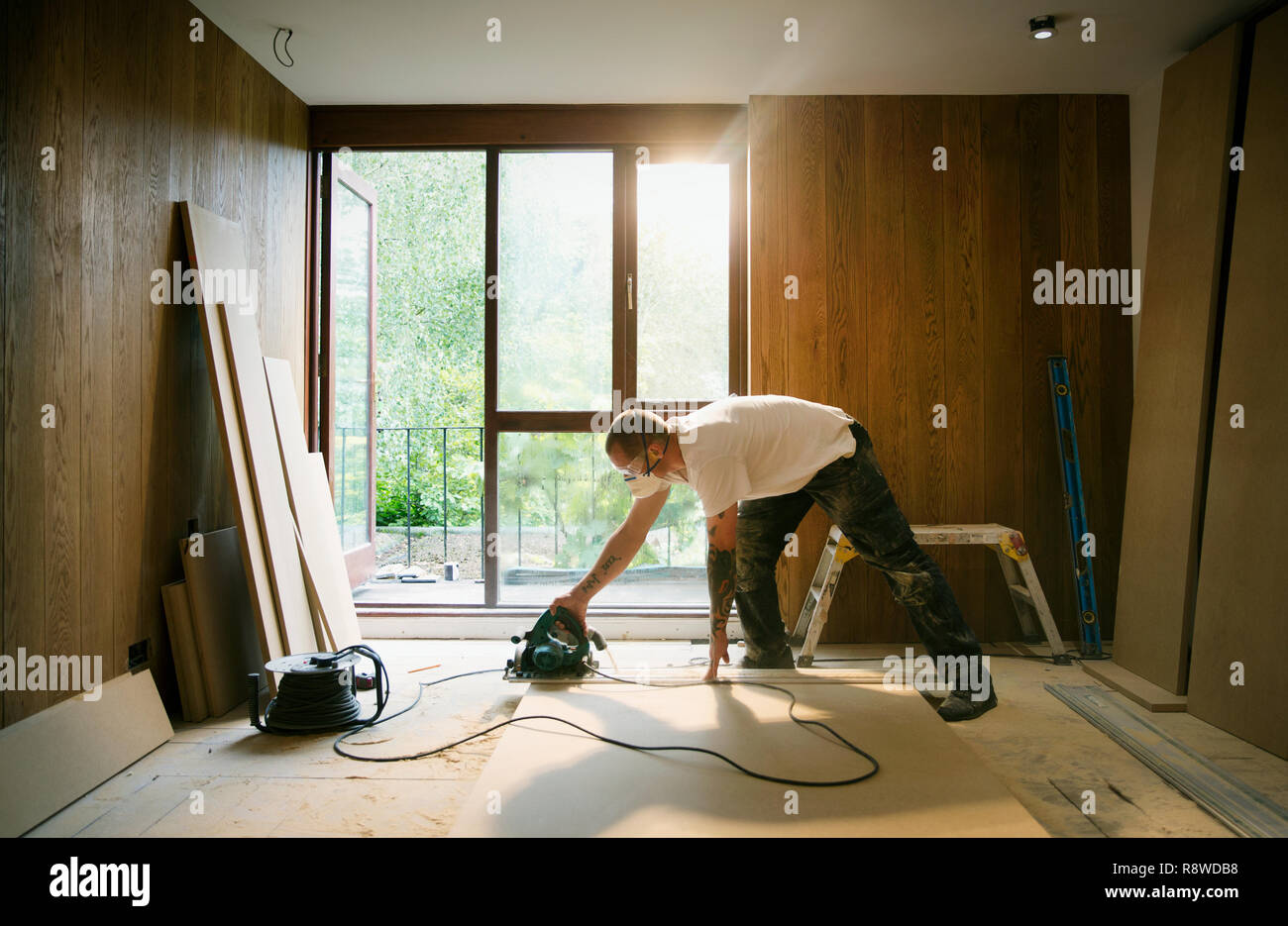 Lavoratore edile con sega elettrica per tagliare il legno in casa Foto Stock