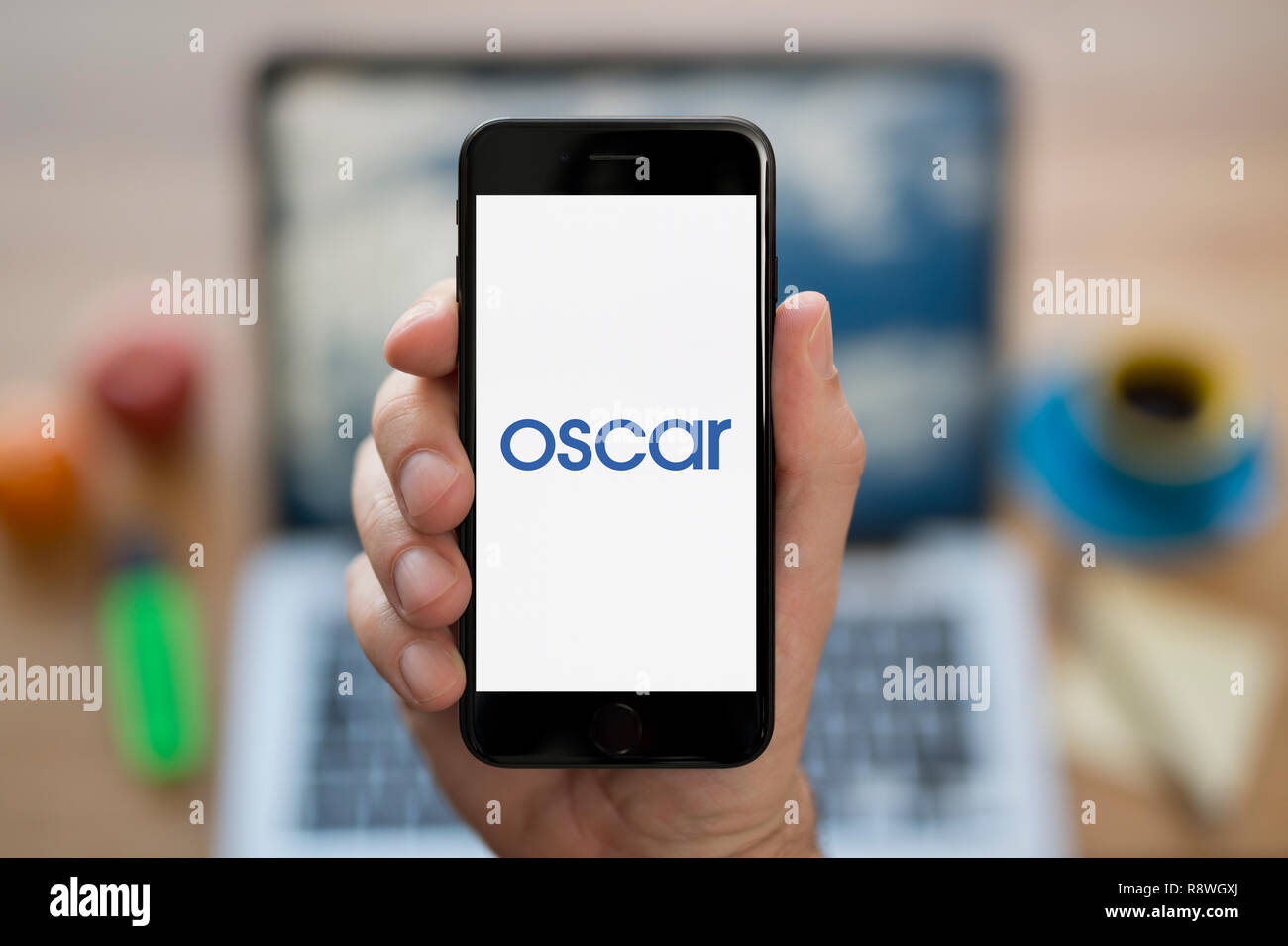 Un uomo guarda al suo iPhone che visualizza il logo di Oscar (solo uso editoriale). Foto Stock