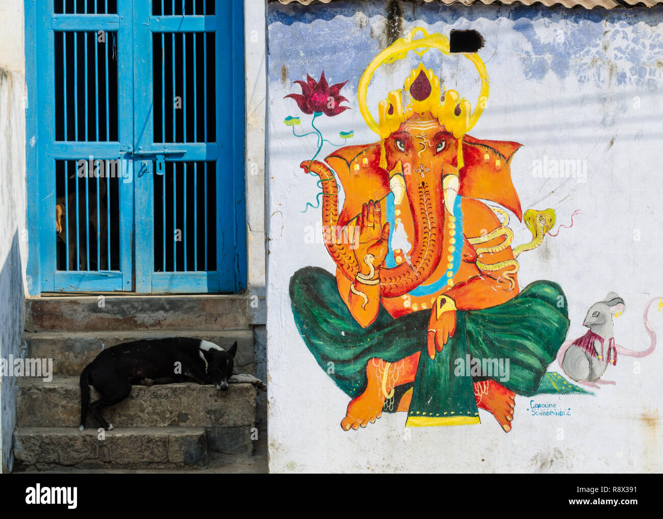 Stray dog dormire sui passi accanto a un Ganesha pittura murale, Varanasi, Uttar Pradesh, India Foto Stock