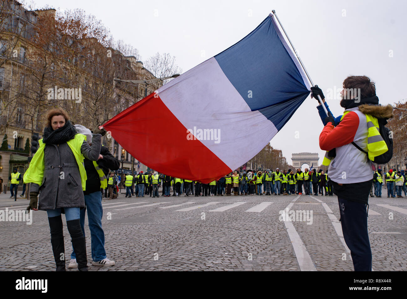 Giubbotti di giallo di dimostrazione (Gilets Jaunes) manifestanti contro le tasse sul carburante, governo e presidente Macron con bandiera a Champs-Élysées, Parigi, Francia Foto Stock