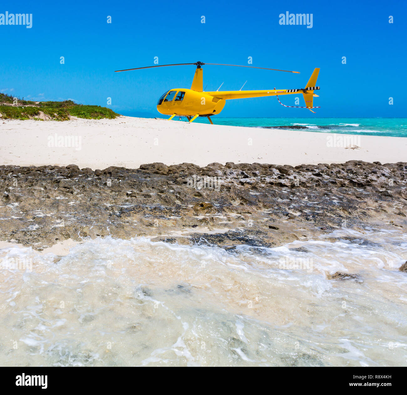 Un elicottero giallo è atterrato su un idilliaco vuoto spiaggia sabbiosa di una remota isola, un azzurro turchese laguna blu in background, Nuova Caledonia, Melanesia. Foto Stock