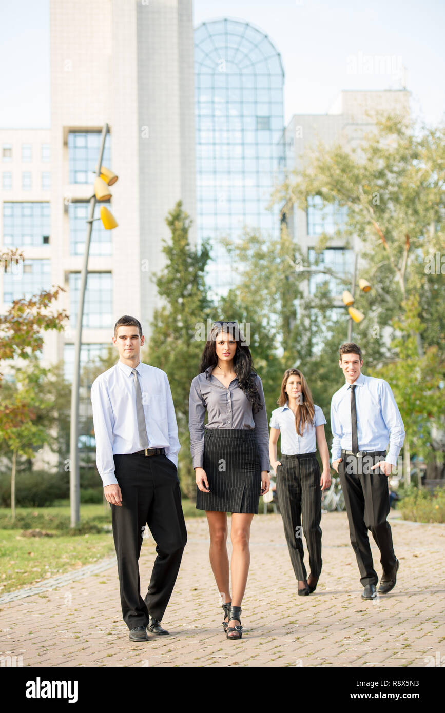 Un gruppo di giovani imprenditori, formalmente vestiti, a piedi attraverso un parco nei pressi della loro azienda. Foto Stock