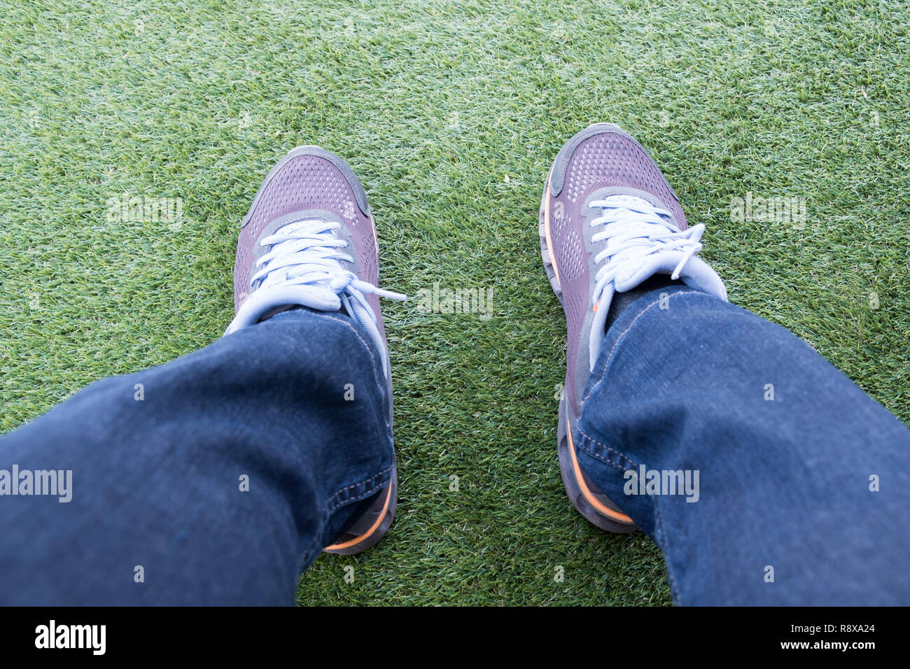 Voce maschile sneaker fuori dei jeans strappati su un verde erba artificiale di un campo da calcio. Foto Stock