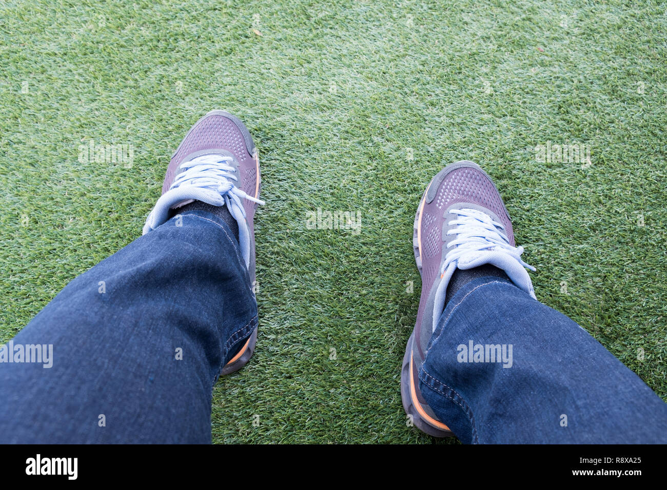 Voce maschile sneaker fuori dei jeans strappati su un verde erba artificiale di un campo da calcio. Foto Stock