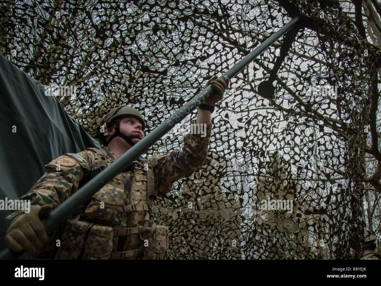 Un soldato lettone del 1 ° brigata lettone luoghi un sondaggio per fissare il camuffamento netting mentre copre un tactical operations center durante l'esercizio Allied spirito vi al settimo Esercito di formazione del comando Hohenfels Area Formazione, Germania, Marzo 15, 2017. Esercizio Allied spirito vi comprende circa 2.770 partecipanti da 12 NATO e partner per la pace delle nazioni, e degli esercizi di tattica di interoperabilità e prove di comunicazione sicura entro i membri dell alleanza e nazioni partner. Foto Stock