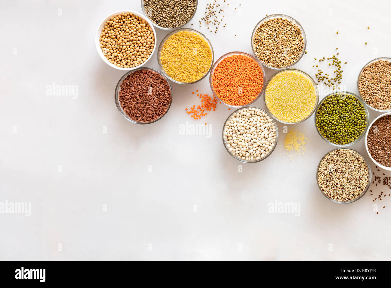 Diagonale laici piana ciotole in vetro con cereali, fagioli e semi su sfondo bianco con copia spazio. Foto Stock