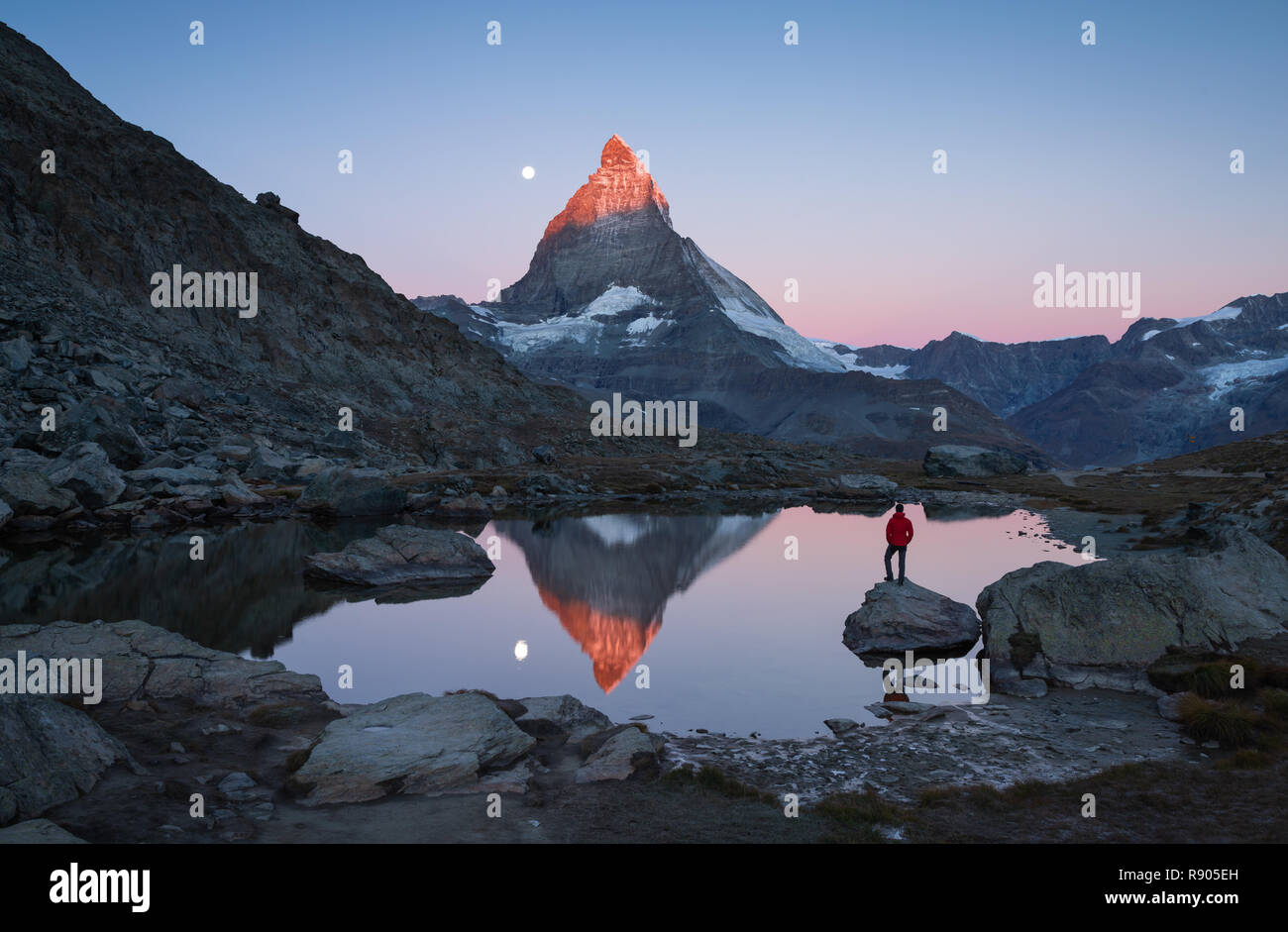Escursionista su una roccia nel Riffelsee all'alba, godendo della vista sul Cervino. Foto Stock