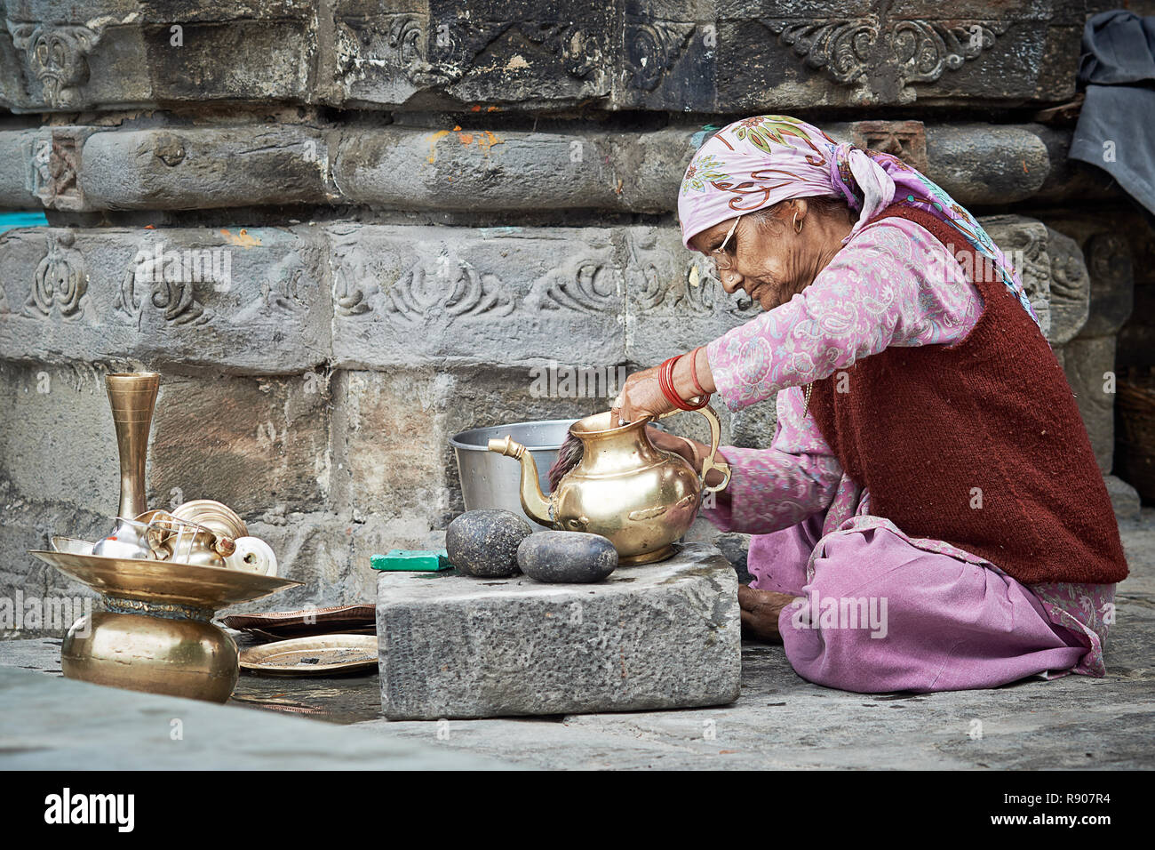 Naggar, India - 17 Luglio: vecchia donna Indiana che pulisce i piatti fuori del tempio. Piatti speciali che fanno offerte a Dio nel tempio. Luglio 17, 2013 Foto Stock