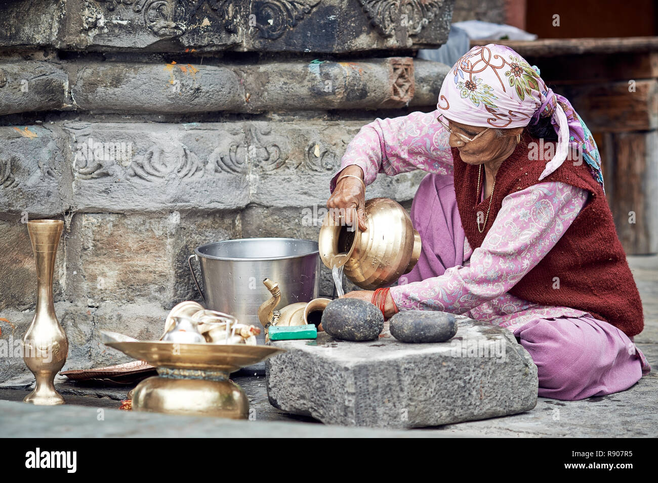 Naggar, India - 17 Luglio: vecchia donna Indiana che pulisce i piatti fuori del tempio. Piatti speciali che fanno offerte a Dio nel tempio. Luglio 17, 2013 Foto Stock