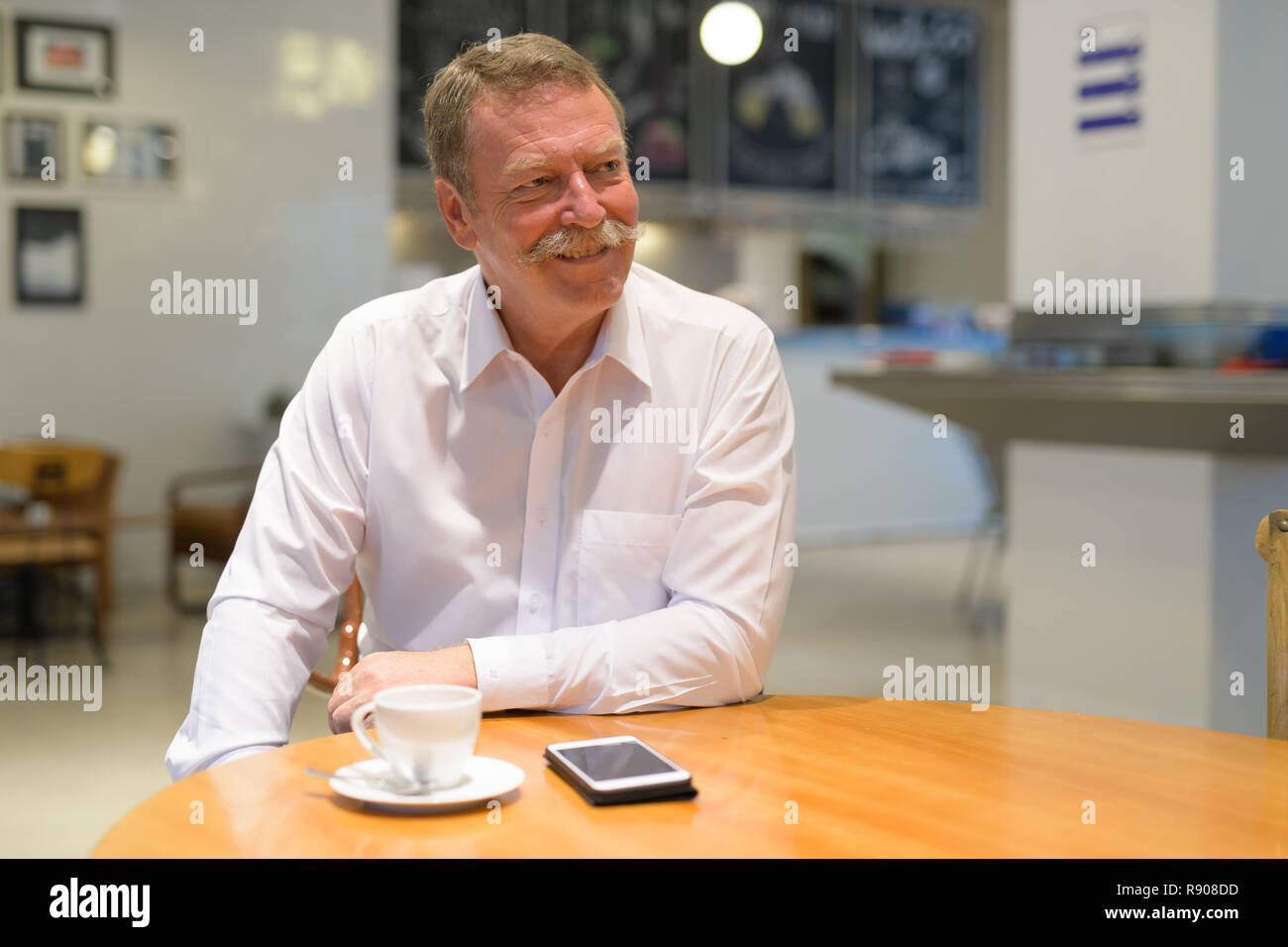 Happy businessman senior seduto e pensando al coffee shop Foto Stock