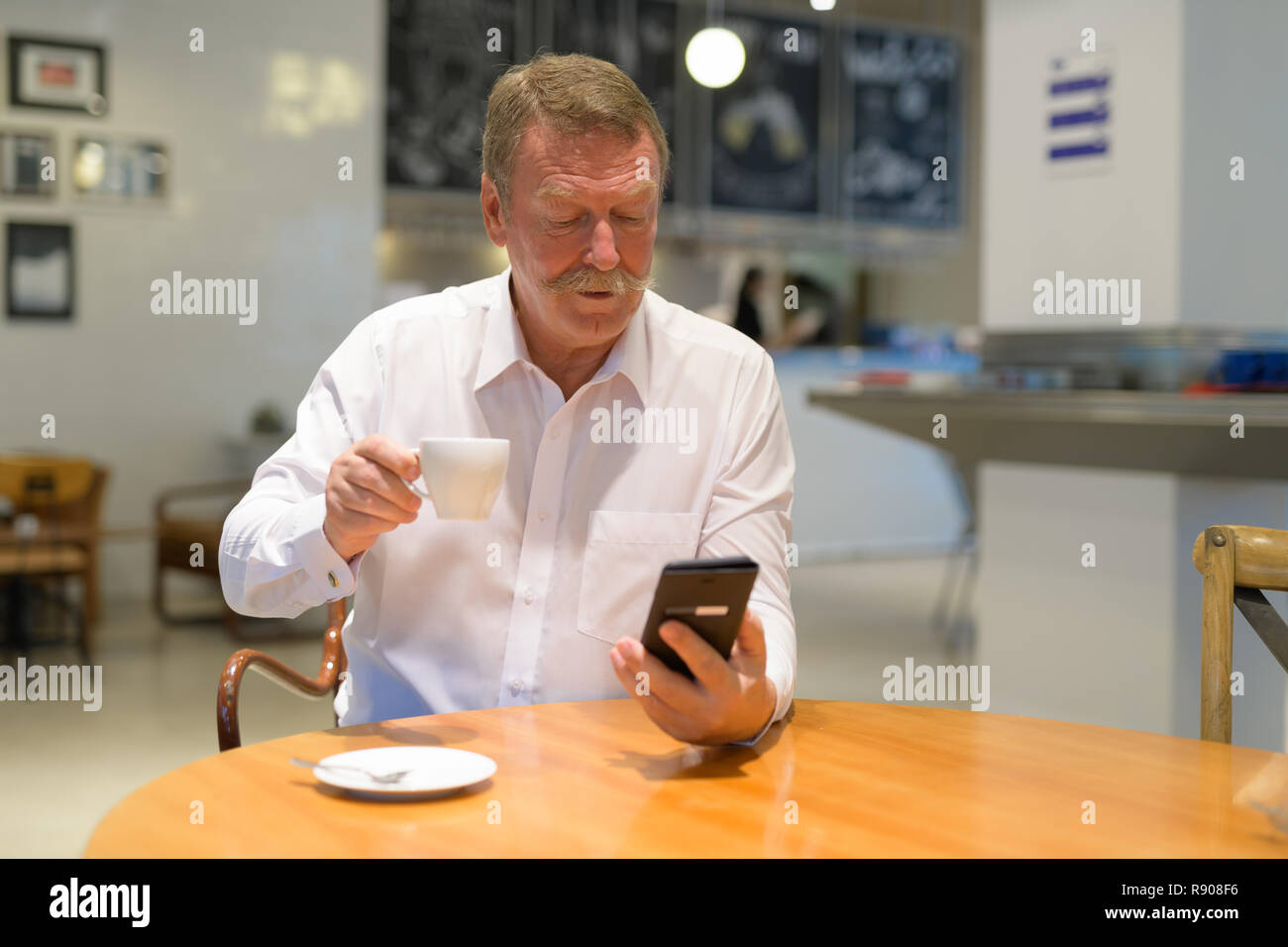 Bello imprenditore senior di bere il caffè mentre usando il telefono Foto Stock