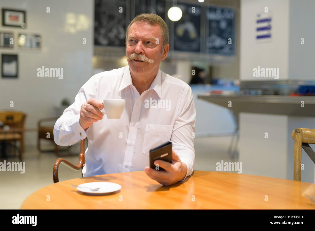 Bello imprenditore senior pensare mentre si beve il caffè e utilizzando il telefono Foto Stock