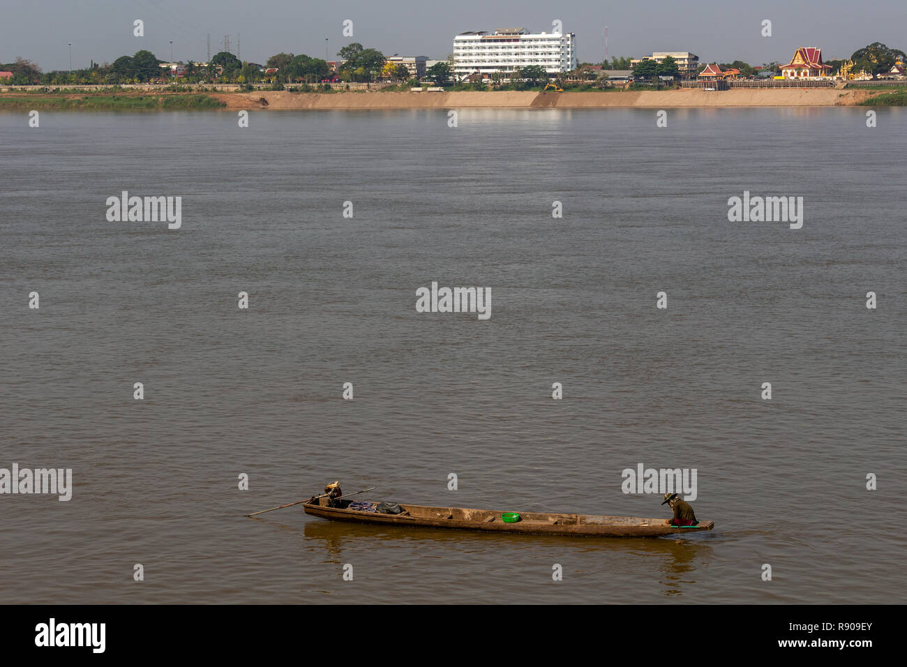 Thakhek, Laos - 19 Aprile 2018: uomo seduto sulla sua barca da pesca nel fiume Mekong al sorgere del sole con la Tailandia in background Foto Stock