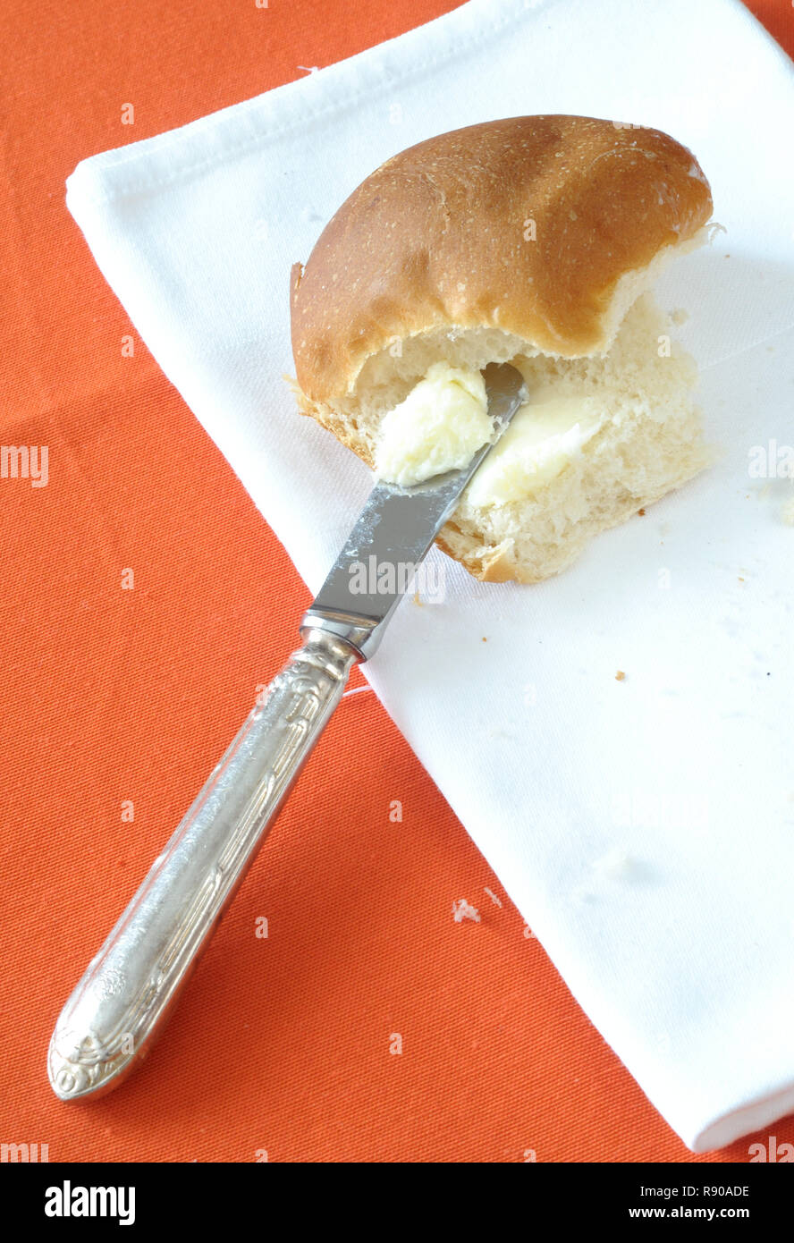 Vista superiore del burro spalmato su un panino, su sfondo arancione, verticale Foto Stock