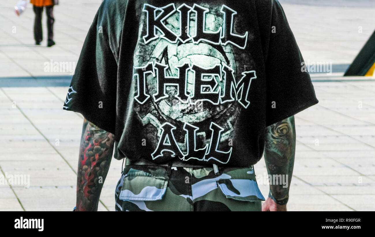 Giovane uomo che indossa pantaloni di mimetizzazione e una t-shirt con un testo che recita: "ucciderli tutti' Foto Stock