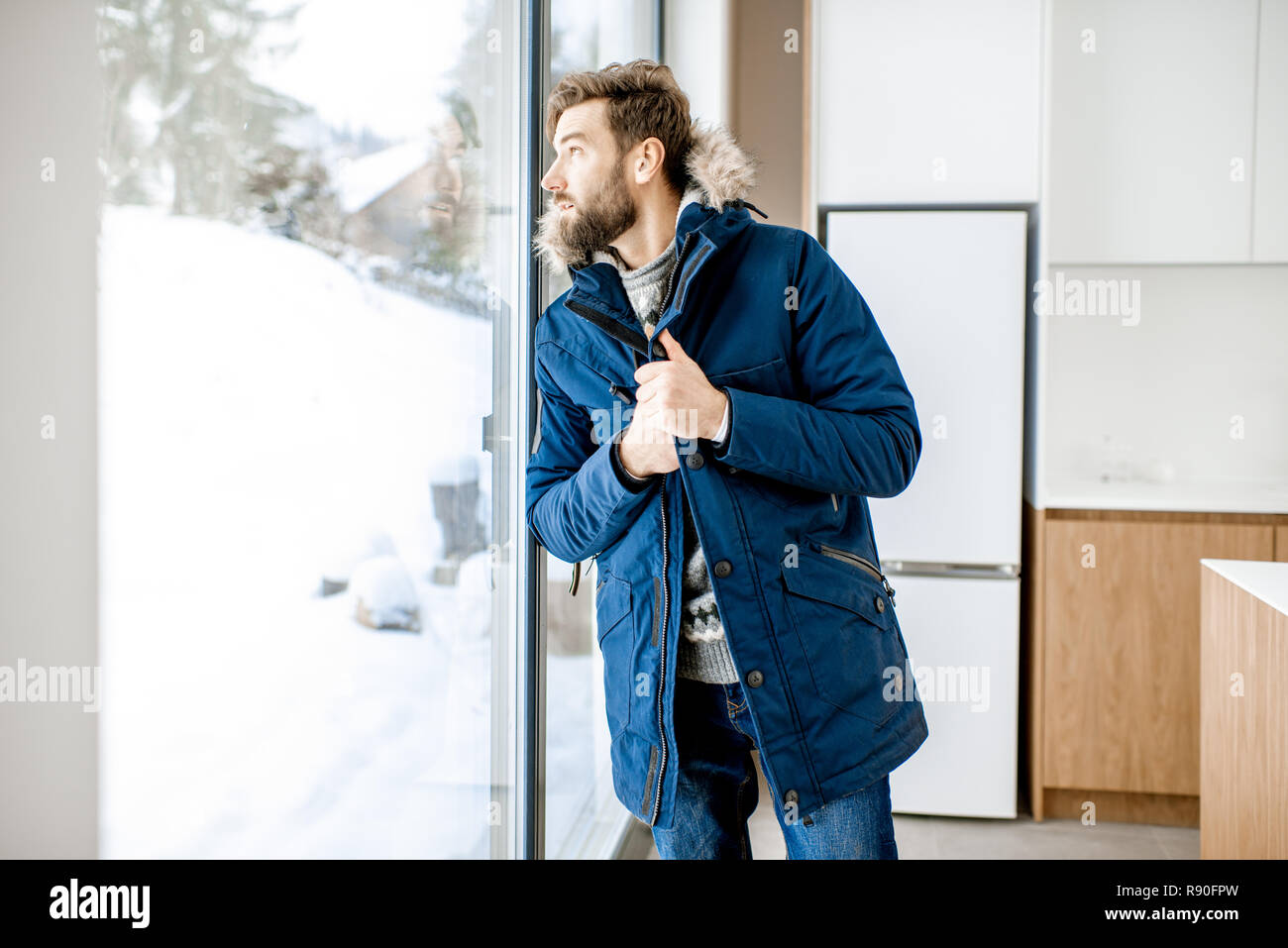 Uomo vestito in abiti invernali la sensazione di freddo in piedi vicino alla finestra a casa senza riscaldamento Foto Stock
