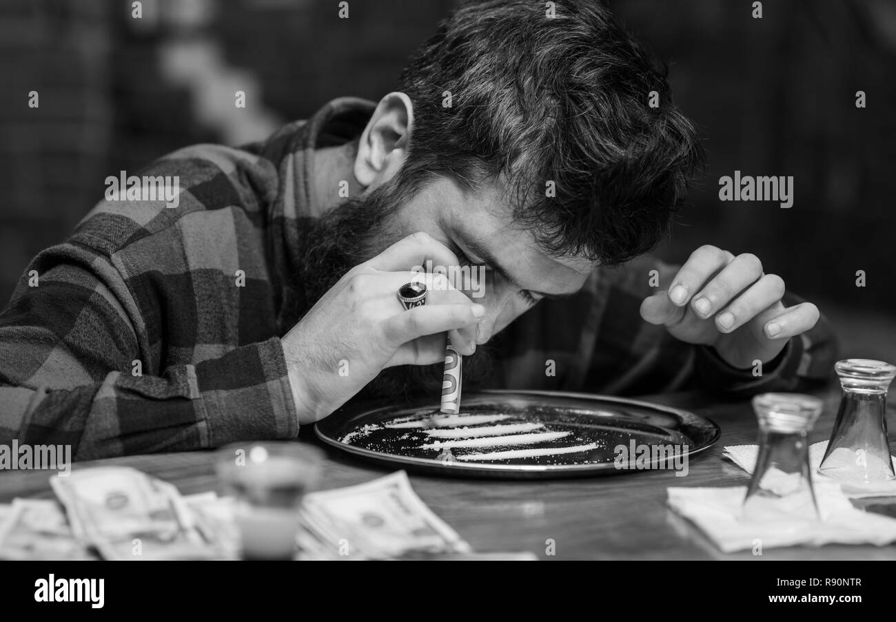 L'uomo con la faccia di occupato da solo al banco bar, lo sniffing di farmaco. Ottenere il concetto di alta. Hipster con la barba sniffs cocaina, farmaco. Guy detiene banconota arrotolata, sfondo sfocato. Foto Stock