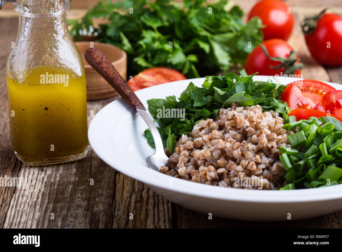 Un sano cotto chicco di grano saraceno con insalata verde fresco cipolla, prezzemolo e pomodori, olio d'oliva e succo di limone condimento, impianti based food, selettivo foc Foto Stock