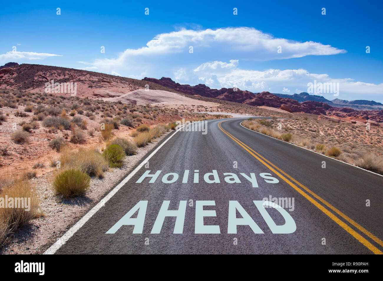 Il testo "Vacanze a venire" scritto su una strada vuota nel deserto del Nevada prima la strada gira a destra Foto Stock