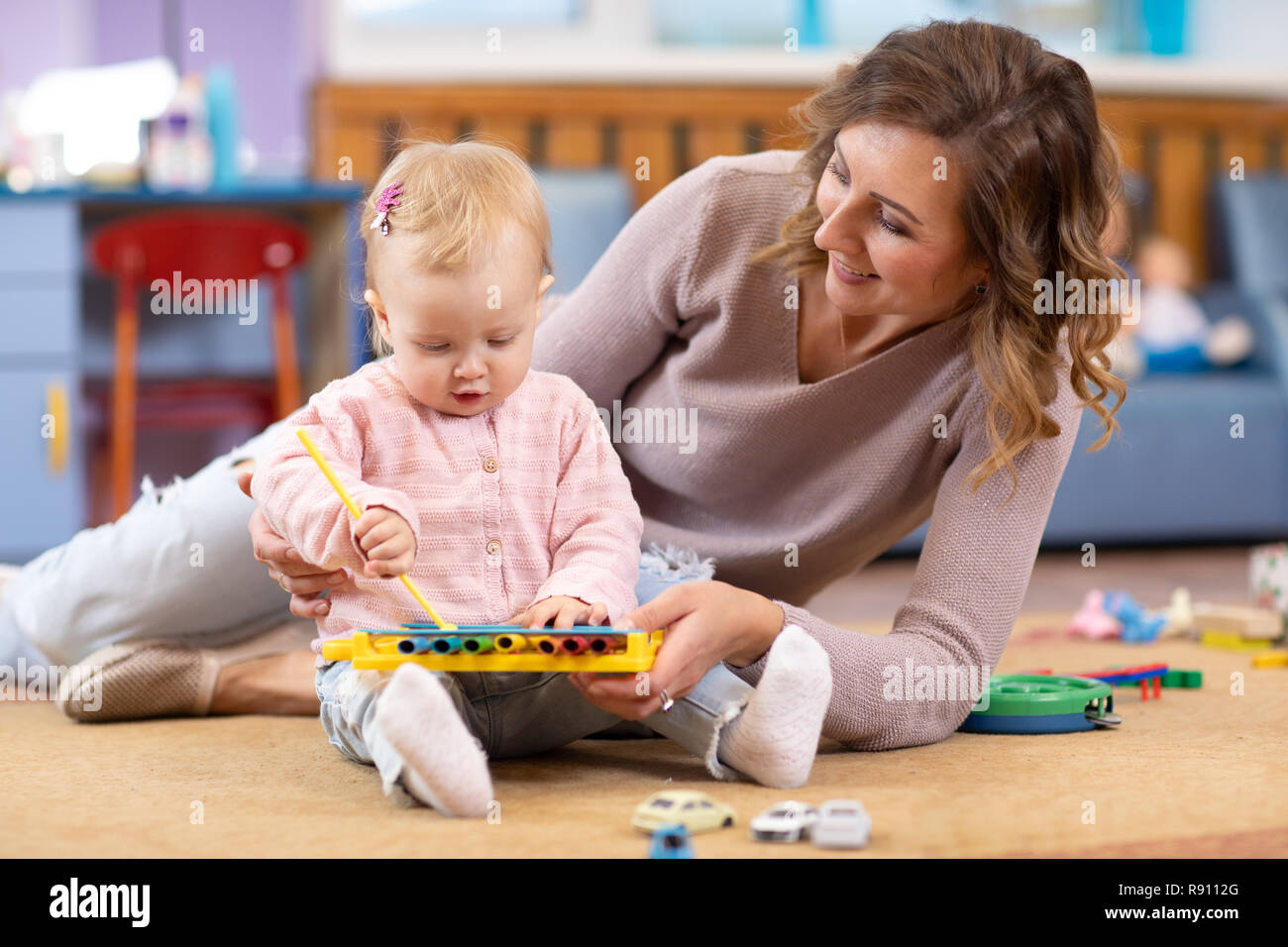 Giovane madre e simpatici baby giocando sul pavimento a casa o in sala  giochi. Mom insegnare la sua bambina come giocare su toy metallophone Foto  stock - Alamy