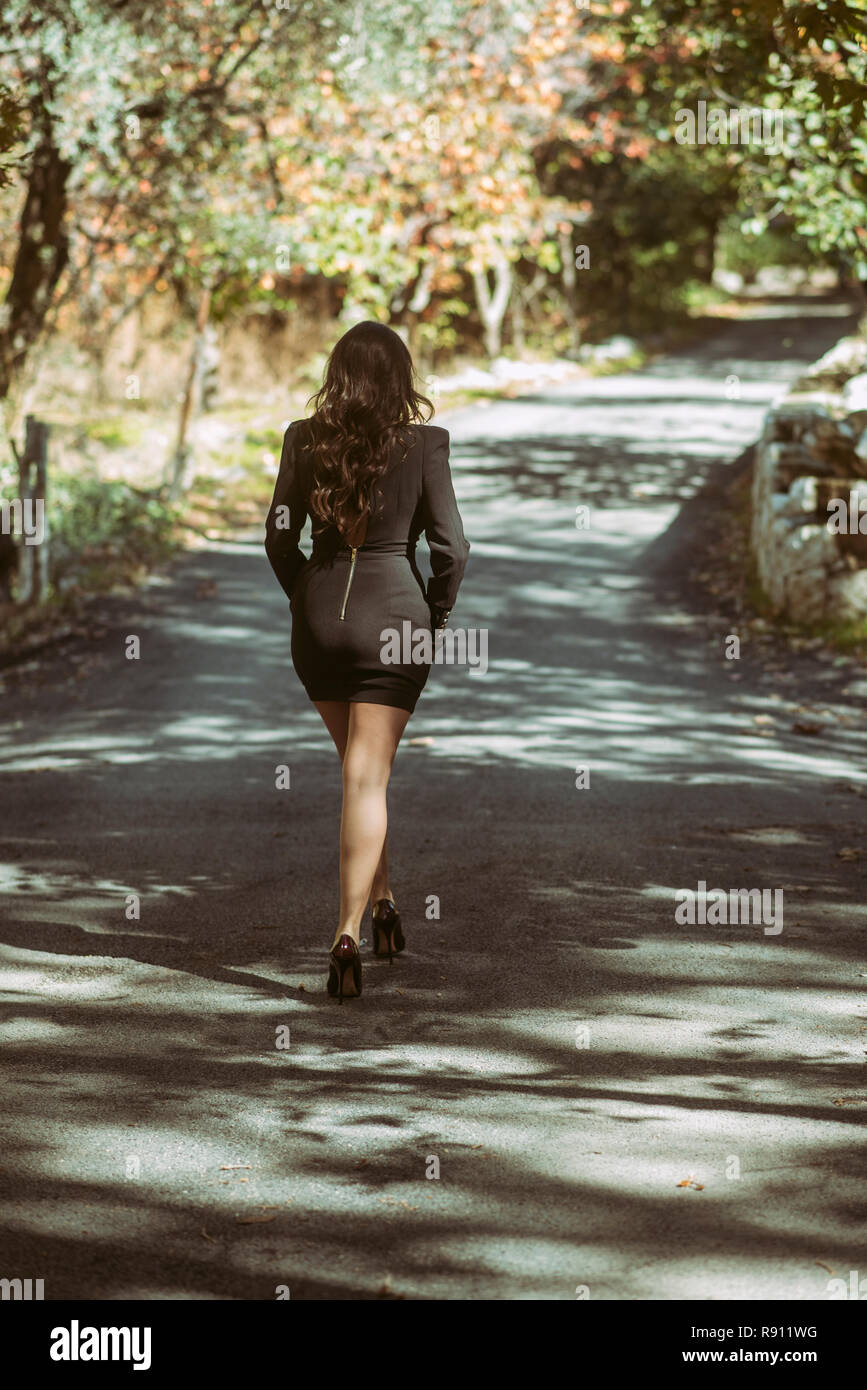 Vista posteriore di una donna che indossa abiti corti e tacchi alti a piedi in campagna Foto Stock