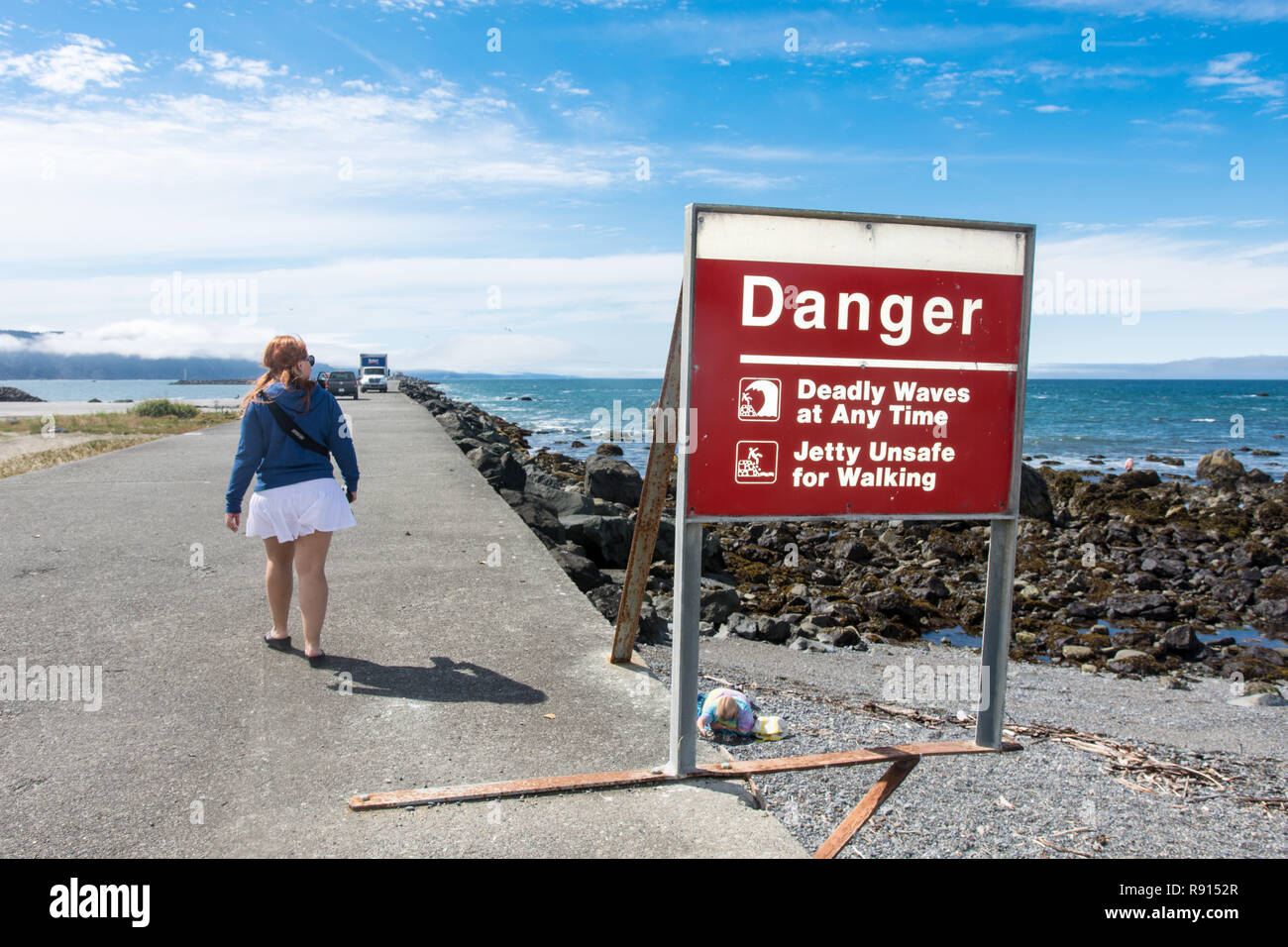 10 Luglio 2017 - Crescent City CA: nonostante il messaggio di avviso sul segno di non camminare a piedi sul molo, un turista femminile ignora il segno, passeggiate sul breakwa Foto Stock