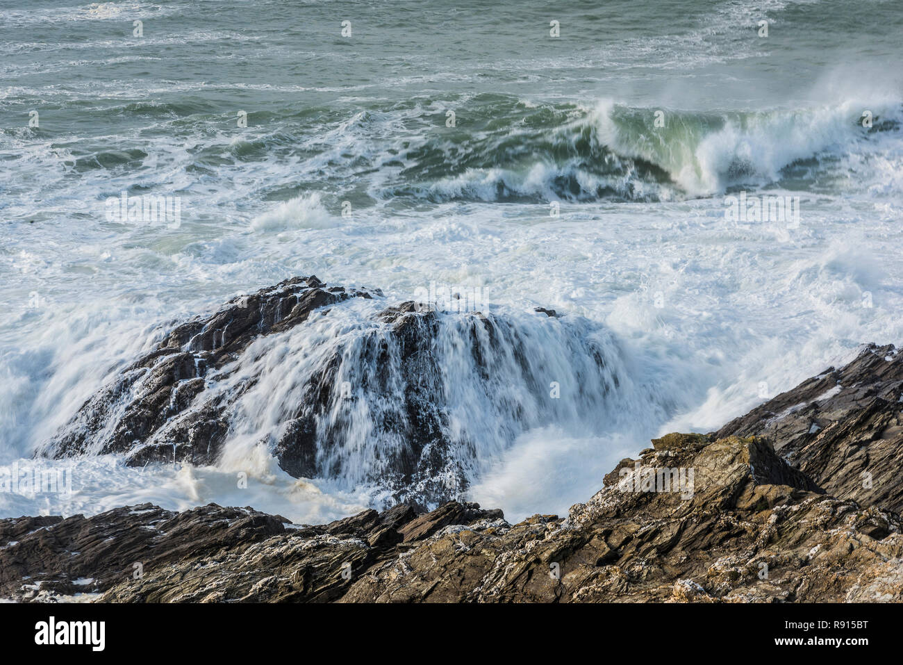 Un ondata di rottura e che scorre su una grande roccia sulla costa di Newquay in Cornovaglia. Foto Stock