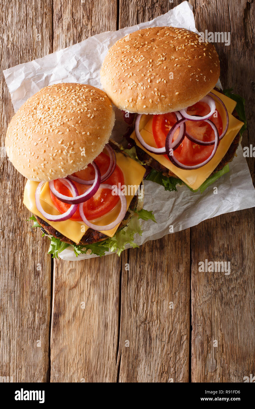 Hamburger Vegetariano con lattuga fresca, cipolle, pomodori e il formaggio cheddar vicino sul tavolo. Verticale in alto vista da sopra Foto Stock
