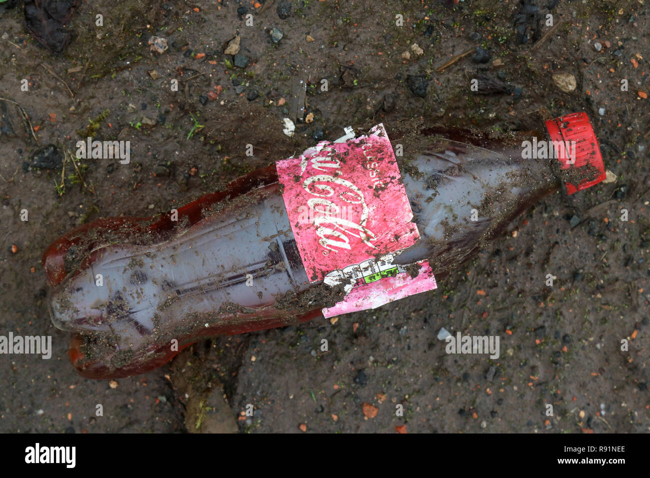 Una sporca in plastica scartata la Coca Cola bottiglia nel fango alla ex fabbrica di IBM sito nella valle Spango, Greenock, Scozia Foto Stock