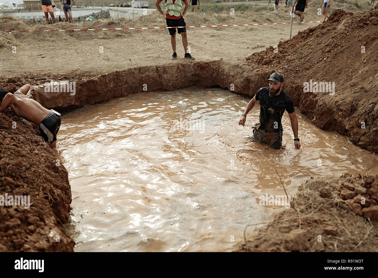 Forte giovane con muscoli passando attraverso la piscina con acqua sporca.abbigliamento sportivo nero sul suo corpo, orologi subacquei sul braccio.concorrenza duro Foto Stock