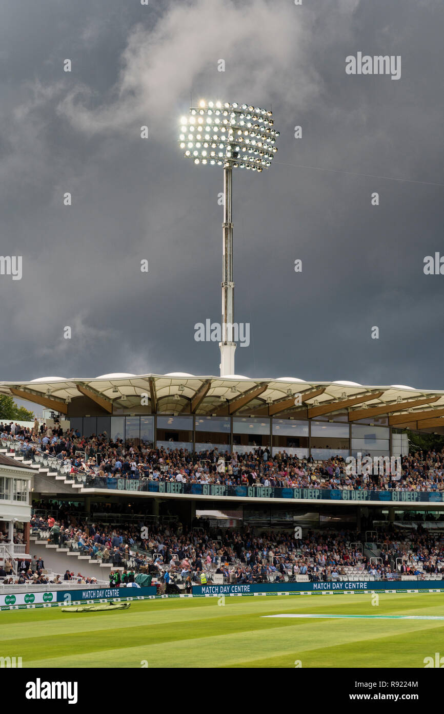 Un proiettore al di sopra della Warner stand al Lords rifulge contro un oscuro meditabondo cielo tempestoso durante il 2018 Inghilterra v India test match Foto Stock