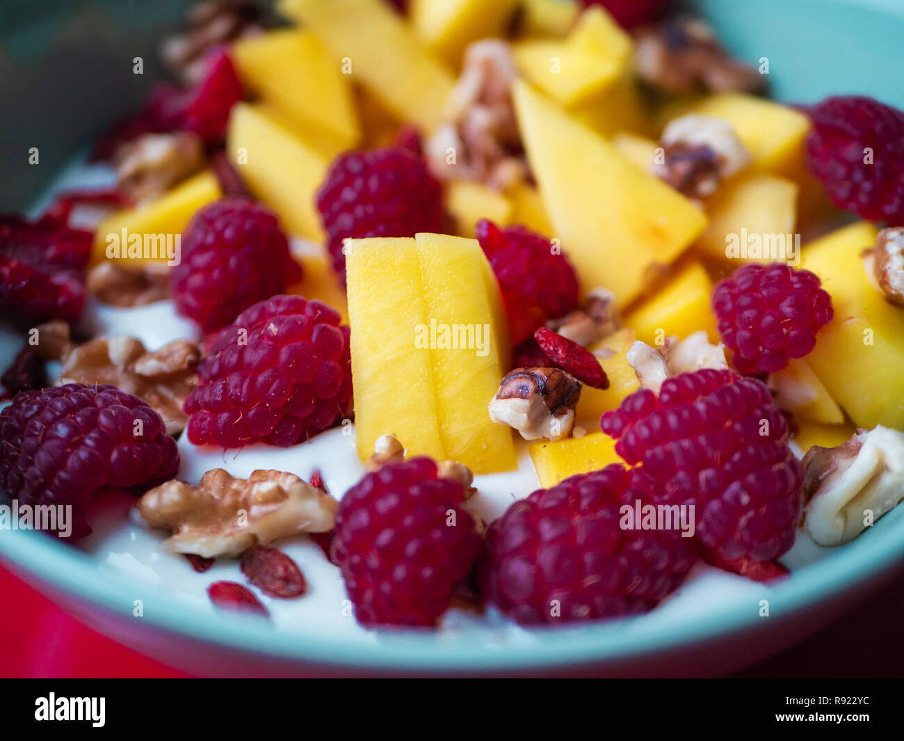 Una deliziosa coppa di frutta con mango, lampone, goji bacche e noci su sfondo rosso Foto Stock