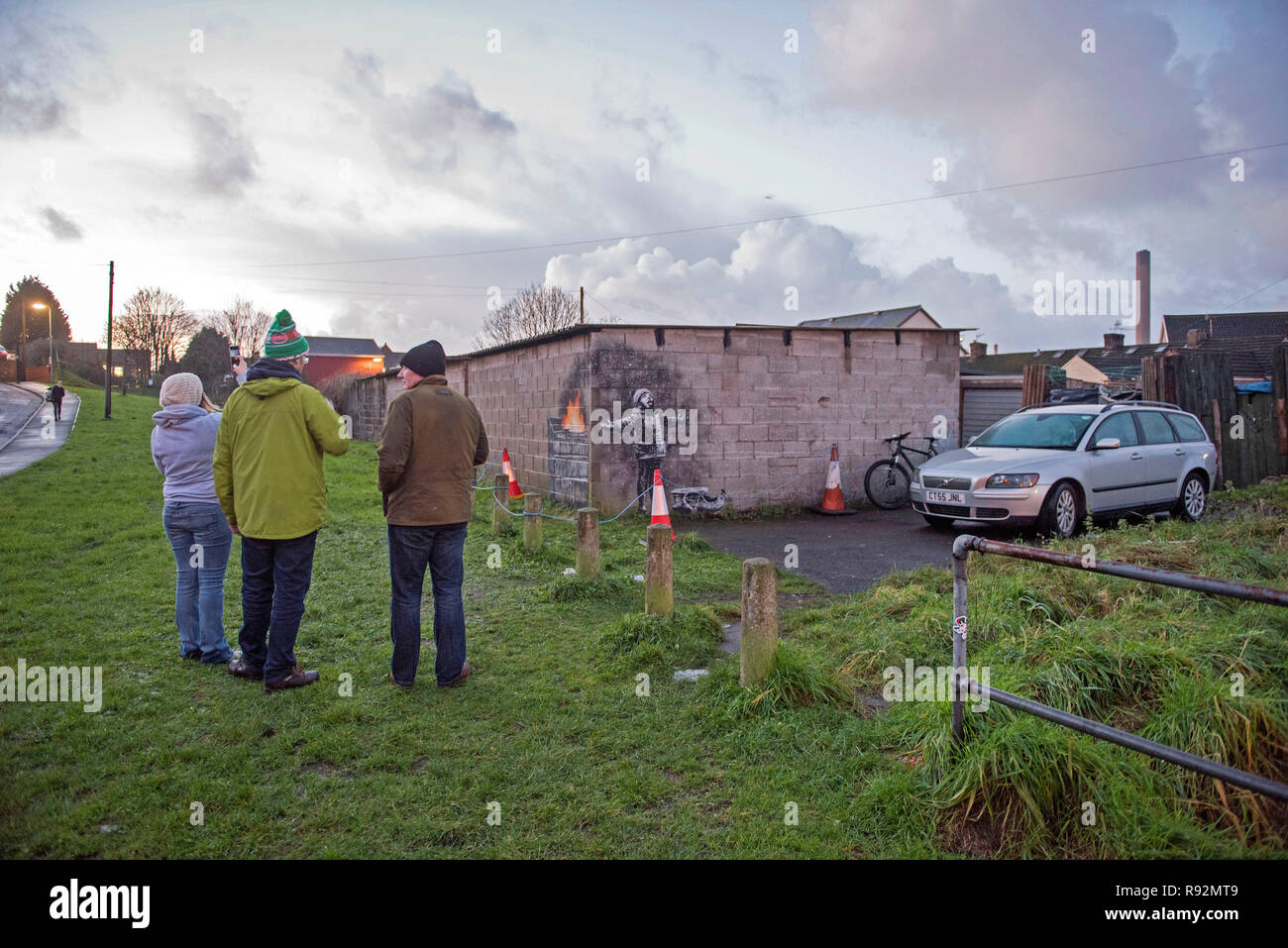 Port Talbot, Wales, Regno Unito. 19 dicembre 2018. I residenti locali di Taibach in Port Talbot ispezionare graffiti che apparve di notte in un garage che è da anonimo artista di strada Banksy. L'illustrazione mostra un bambino con le braccia aperte in riproduzione in ciò che sembra essere la neve con una slitta al suo fianco, ma l'altro lato della parete rivela è una cenere da un cestino della spazzatura sul fuoco. Credito: Phil Rees/Alamy Live News Foto Stock