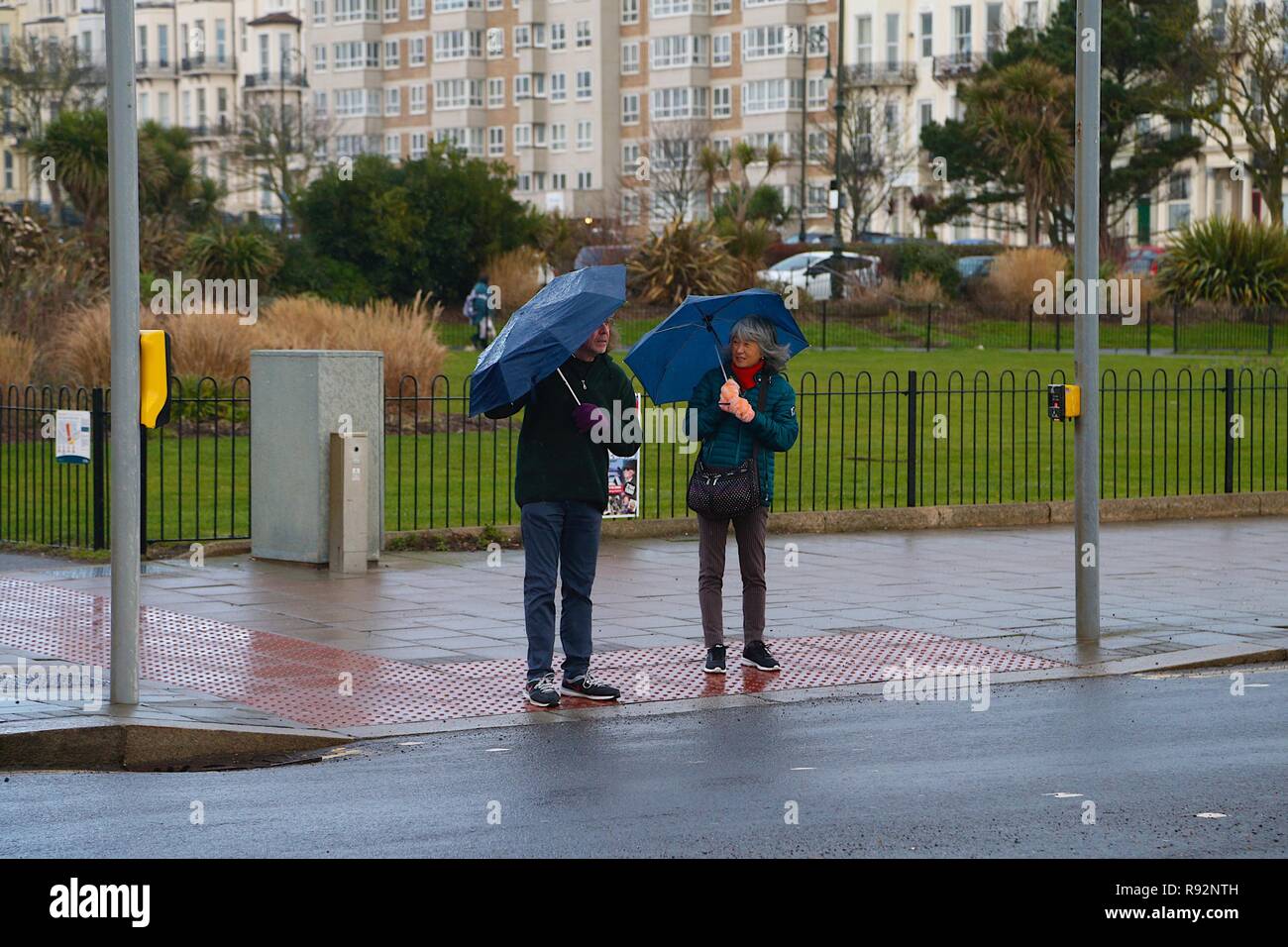 Hastings, East Sussex, Regno Unito. 19 Dic, 2018. Regno Unito: Meteo acquazzoni pesanti di pioggia sono attesi durante tutta la giornata in Hastings, East Sussex come le perturbazioni atmosferiche continua. Una coppia di anziani attendere a un attraversamento pedonale ombrelli azienda sotto la pioggia. © Paul Lawrenson 2018, Photo credit: Paolo Lawrenson / Alamy Live News Foto Stock