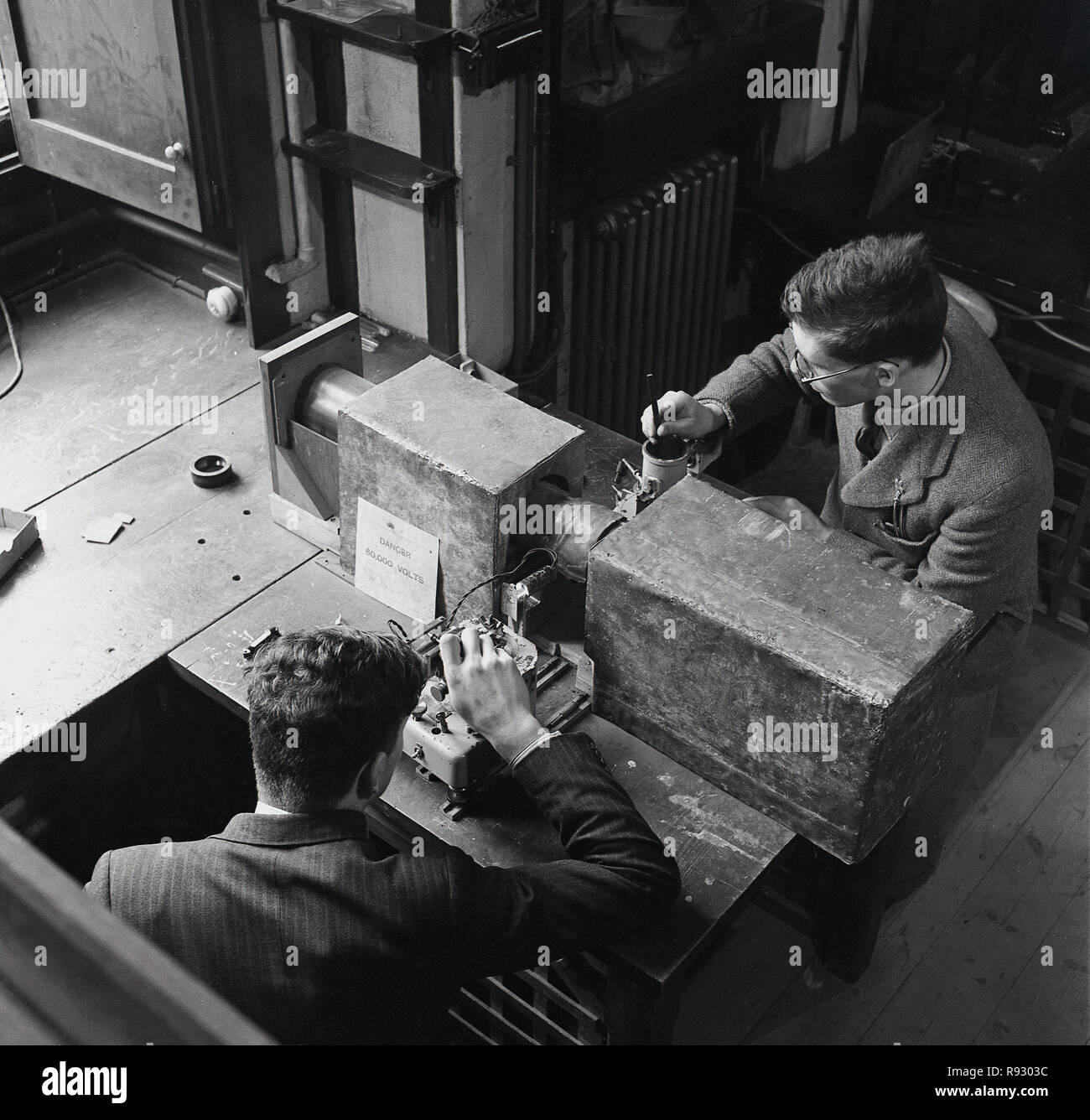 Degli anni Cinquanta, Oxford University, vista aerea di due uomini di scienza agli studenti di condurre esperimenti che misurano la tensione con metri e appositamente realizzato il tubo e scatola in legno di copertura. Visto nella foto è un segno che dice "ira 60.000 volt" Foto Stock