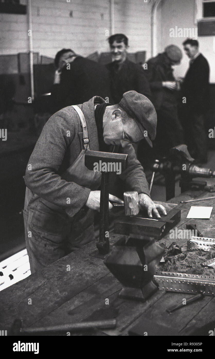 Anni quaranta, storici, lavoratori delle miniere rioccupati in un laboratorio, Merthyr. Galles, con un lavoratore maschio in un tappo di stoffa ad una panca di legno che fa il metallo lavoro, facendo piatti di metallo. Foto Stock