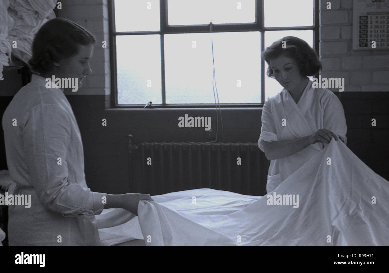 1940s, storico, due dei lavoratori di sesso femminile in bianco-cappotti lavorando in un sintetico della fabbrica di seta la piegatura a mano un rayon o poliestere lenzuolo, South Wales, Regno Unito. Foto Stock